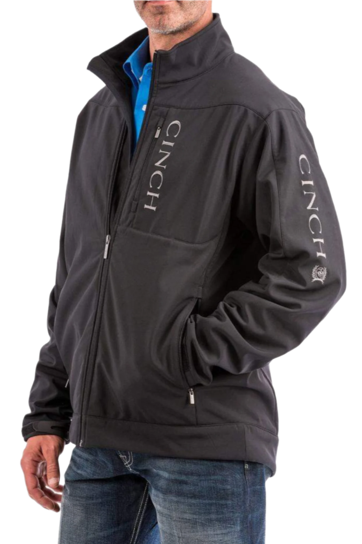 Man wearing a black Cinch softshell jacket with CINCH branding down the sleeve and jeans, hands in pockets
