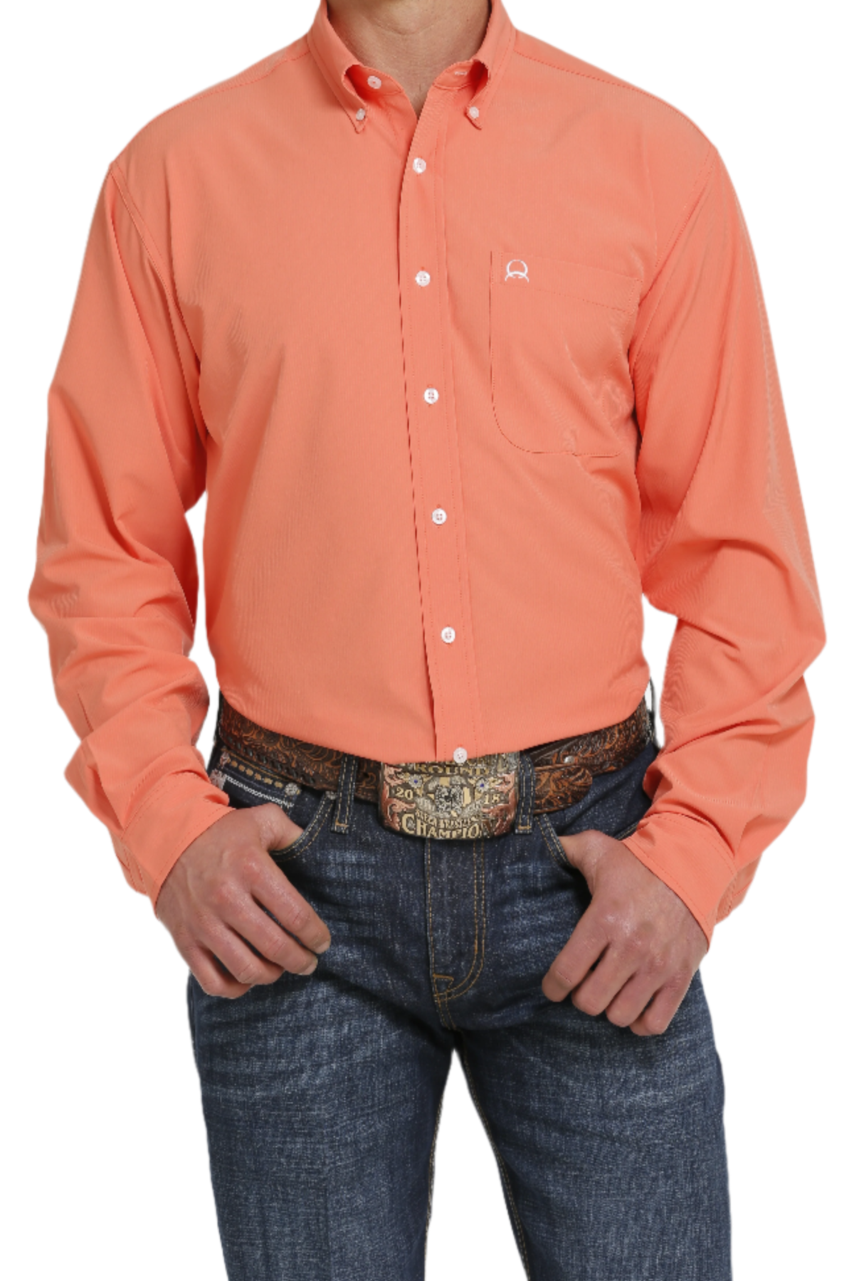 A man wearing a coral long-sleeve button-down shirt and blue jeans. The shirt is tucked into the jeans, and the man is wearing a belt with a decorative buckle.