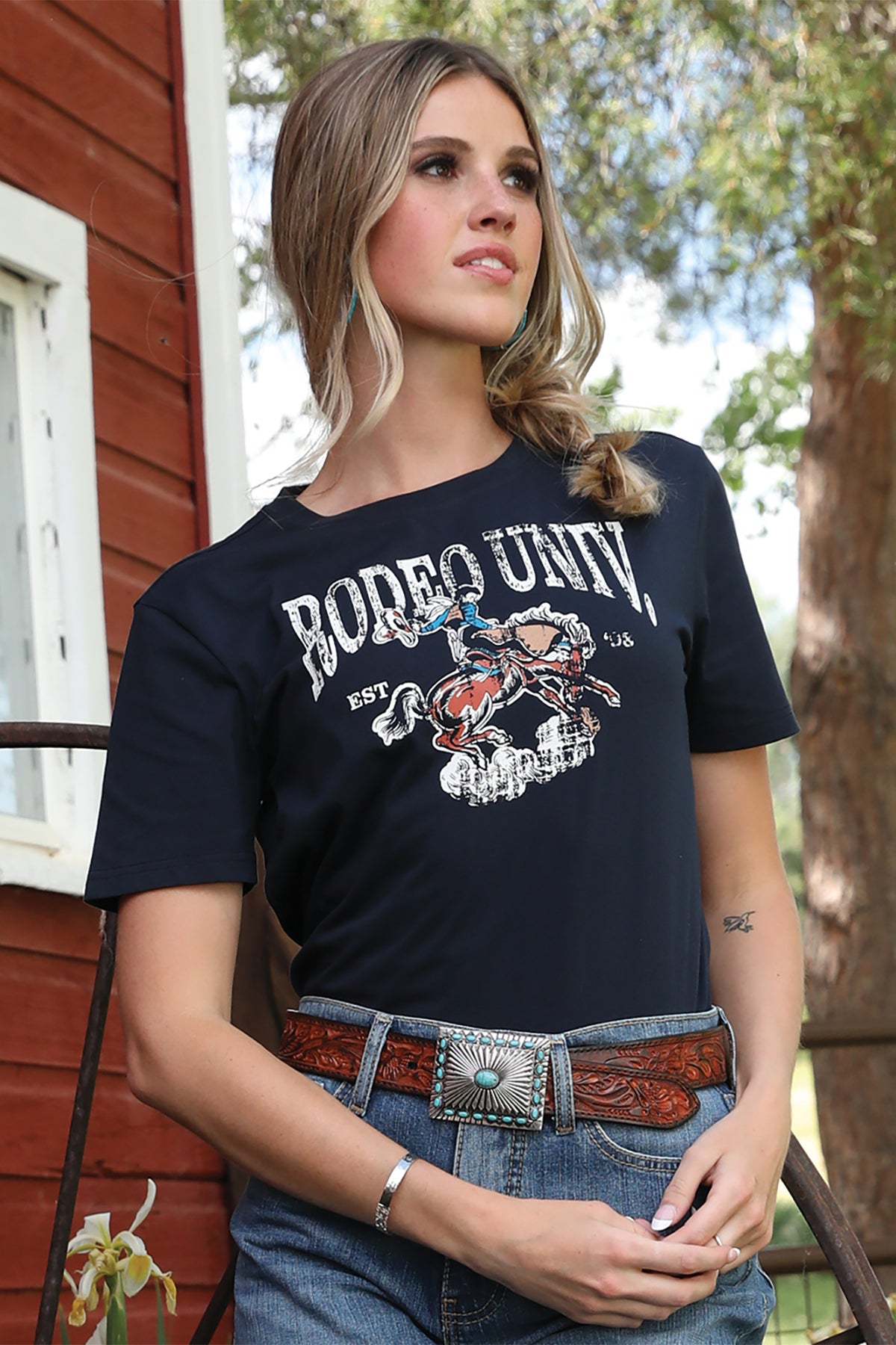 Woman wearing a black 'Rodeo University' t-shirt outdoors.
