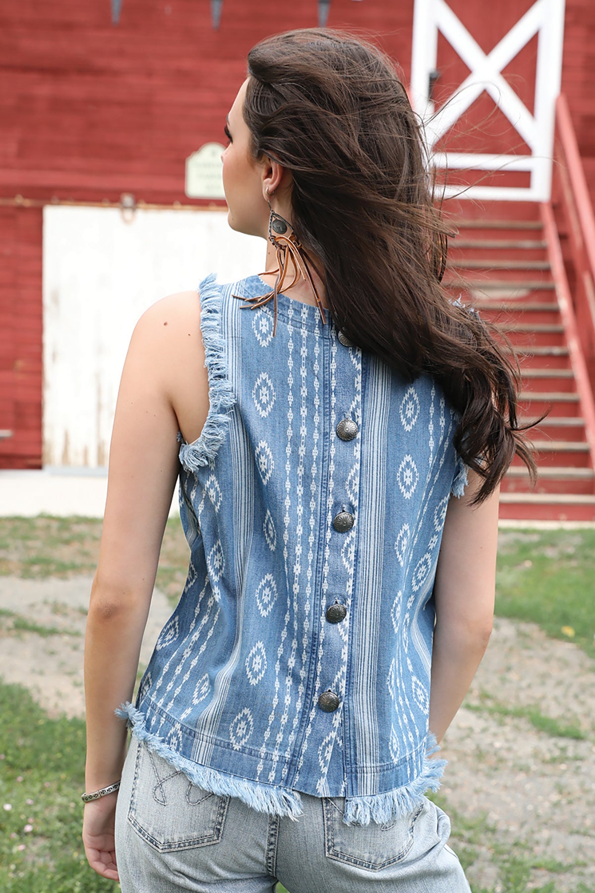 Back view of a girl standing in front of a barn wearing a light blue tank top and jeans