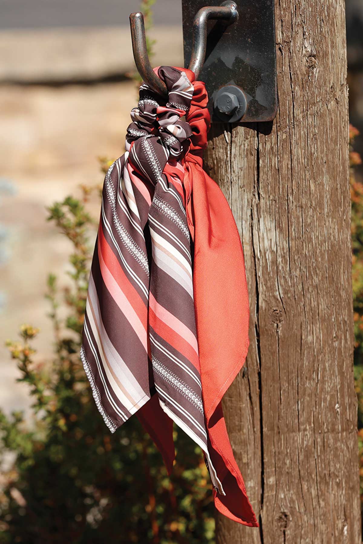 Colorful striped scarf draped over a metal hook on a wooden post with a blurred natural background.