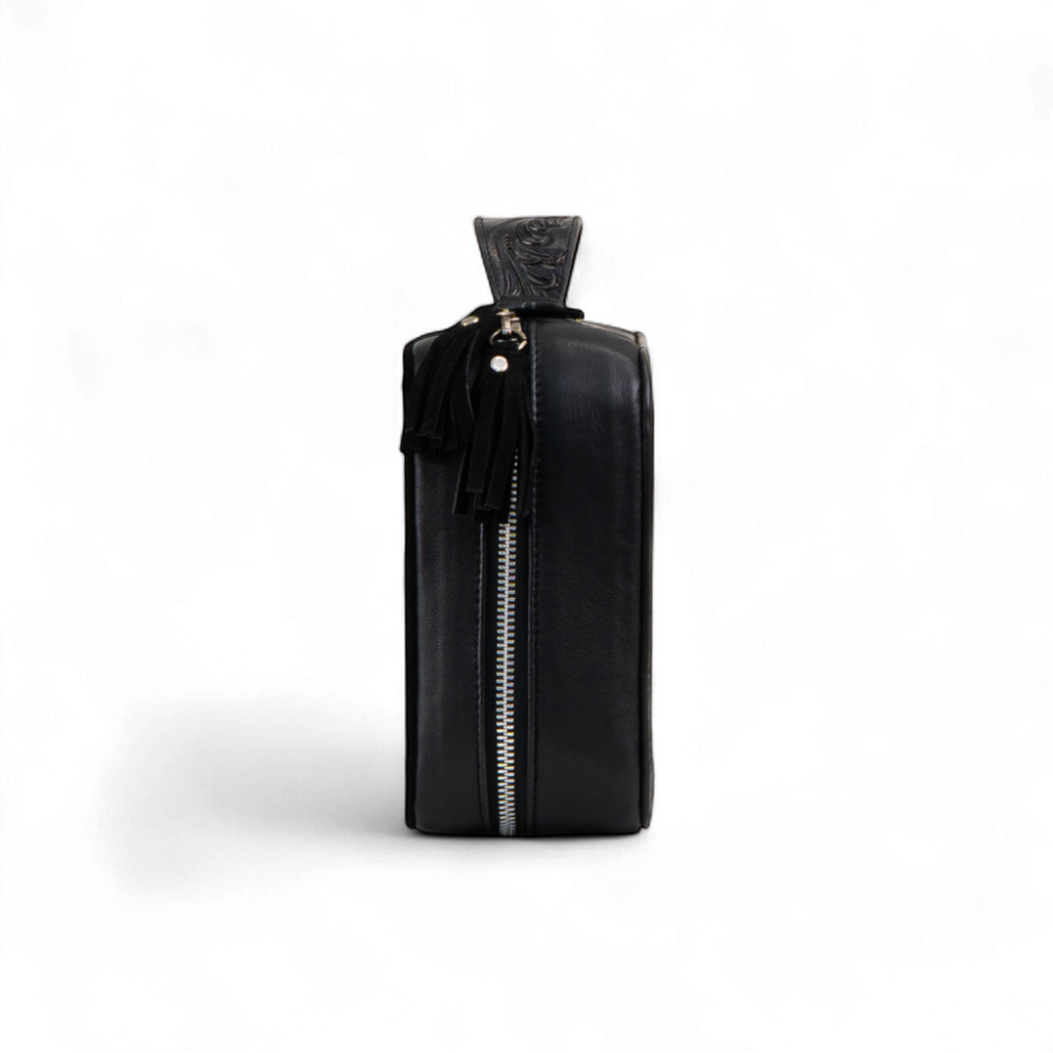 Black rectangular toiletry bag shown from the side, featuring a full-length silver zipper and a tooled leather pull tab with tassel accents