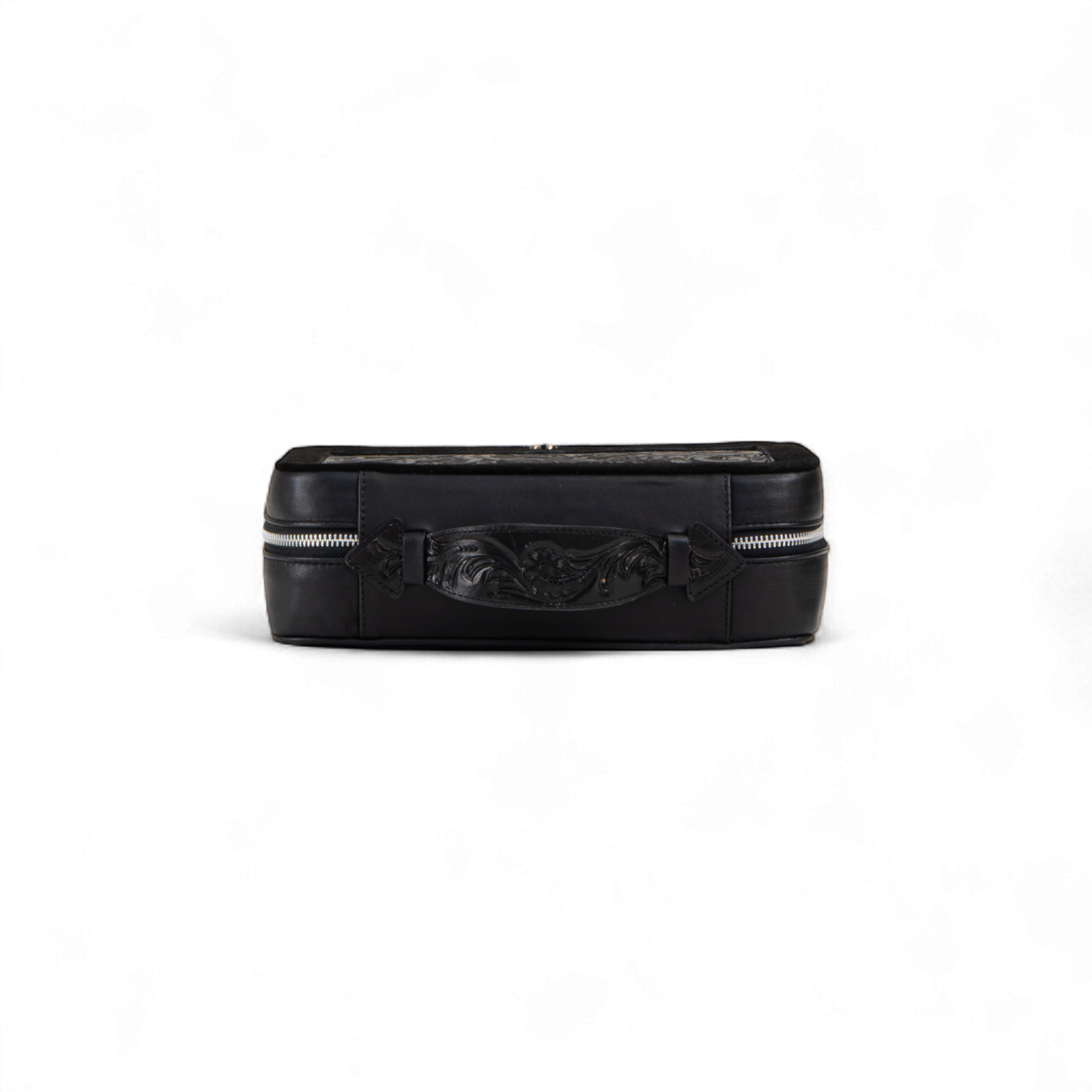 Black rectangular toiletry bag shown from the side, featuring a tooled leather handle in the center and silver zipper details on both ends