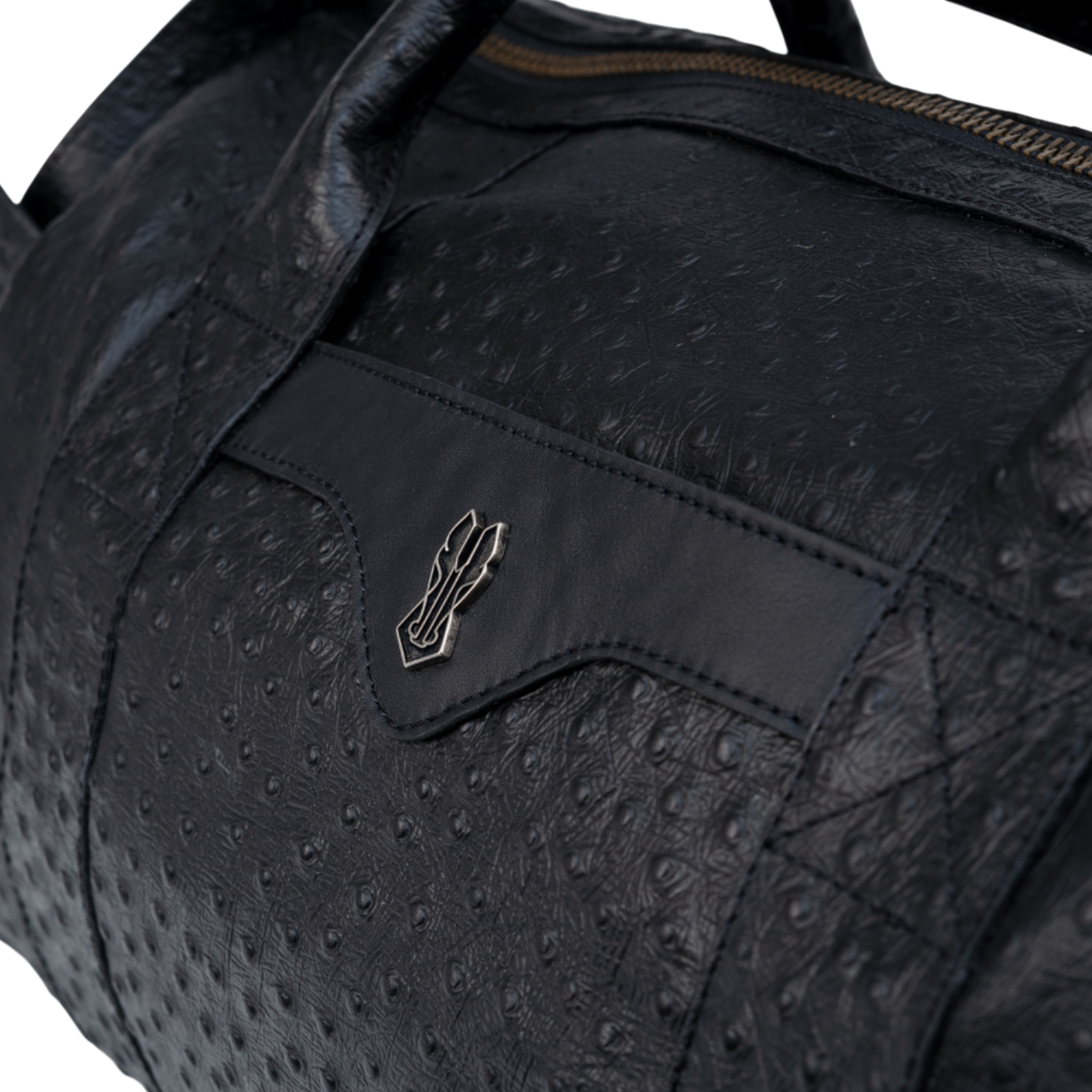 Close-up of a black bag featuring a textured ostrich-print leather pattern and a smooth leather accent with a small metallic emblem in the center