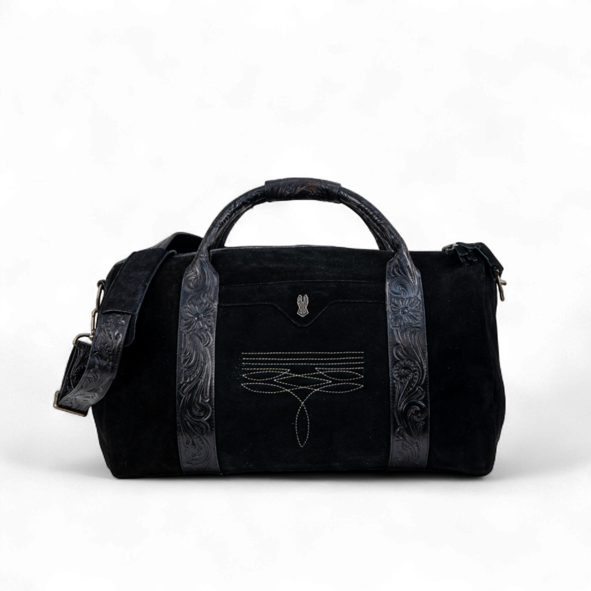 Black suede duffel bag with tooled leather handles and trim, featuring decorative stitching on the front panel. The bag includes an adjustable shoulder strap and a structured silhouette