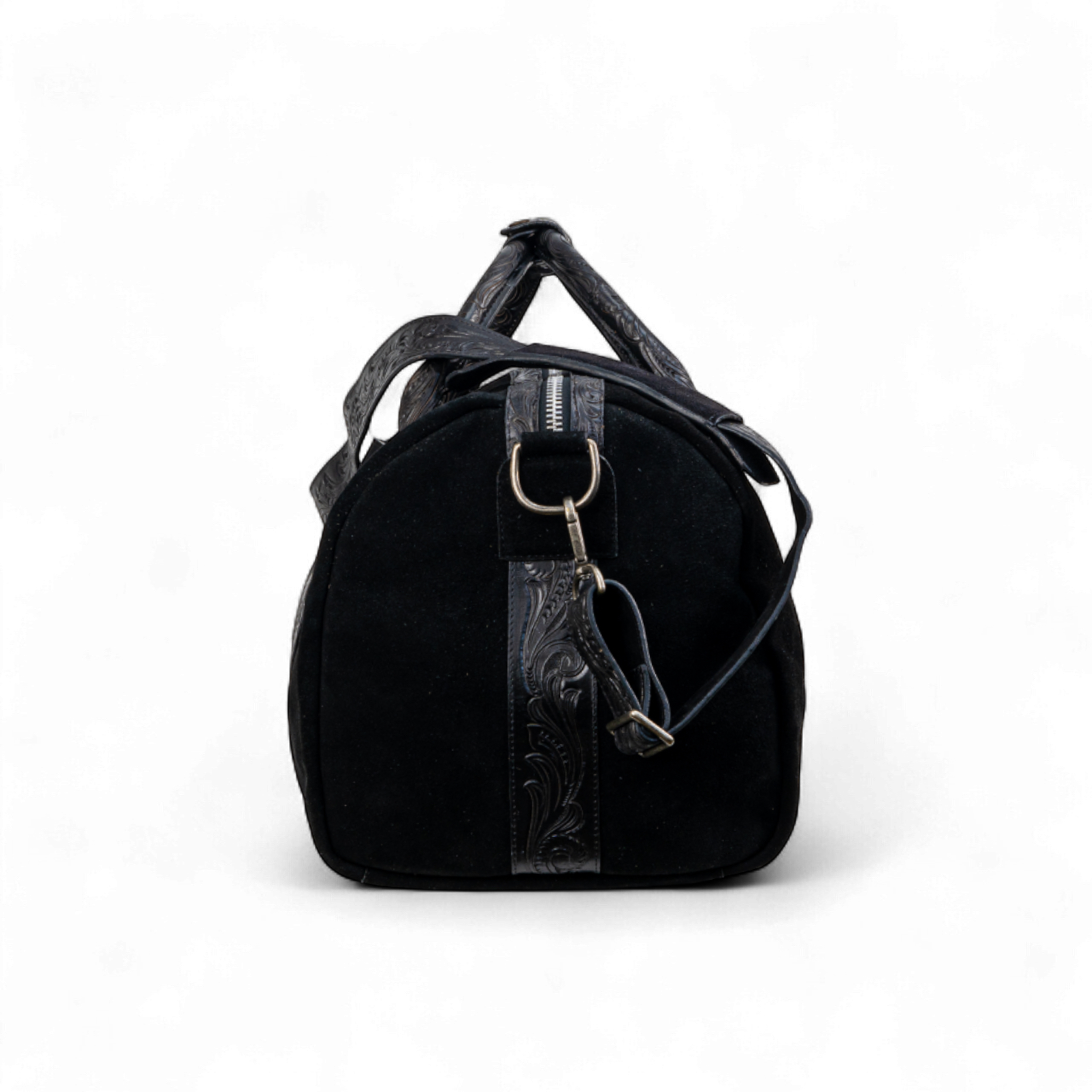 Side view of a black suede duffel bag, featuring a tooled leather strap detail with a metal D-ring and an attached adjustable shoulder strap