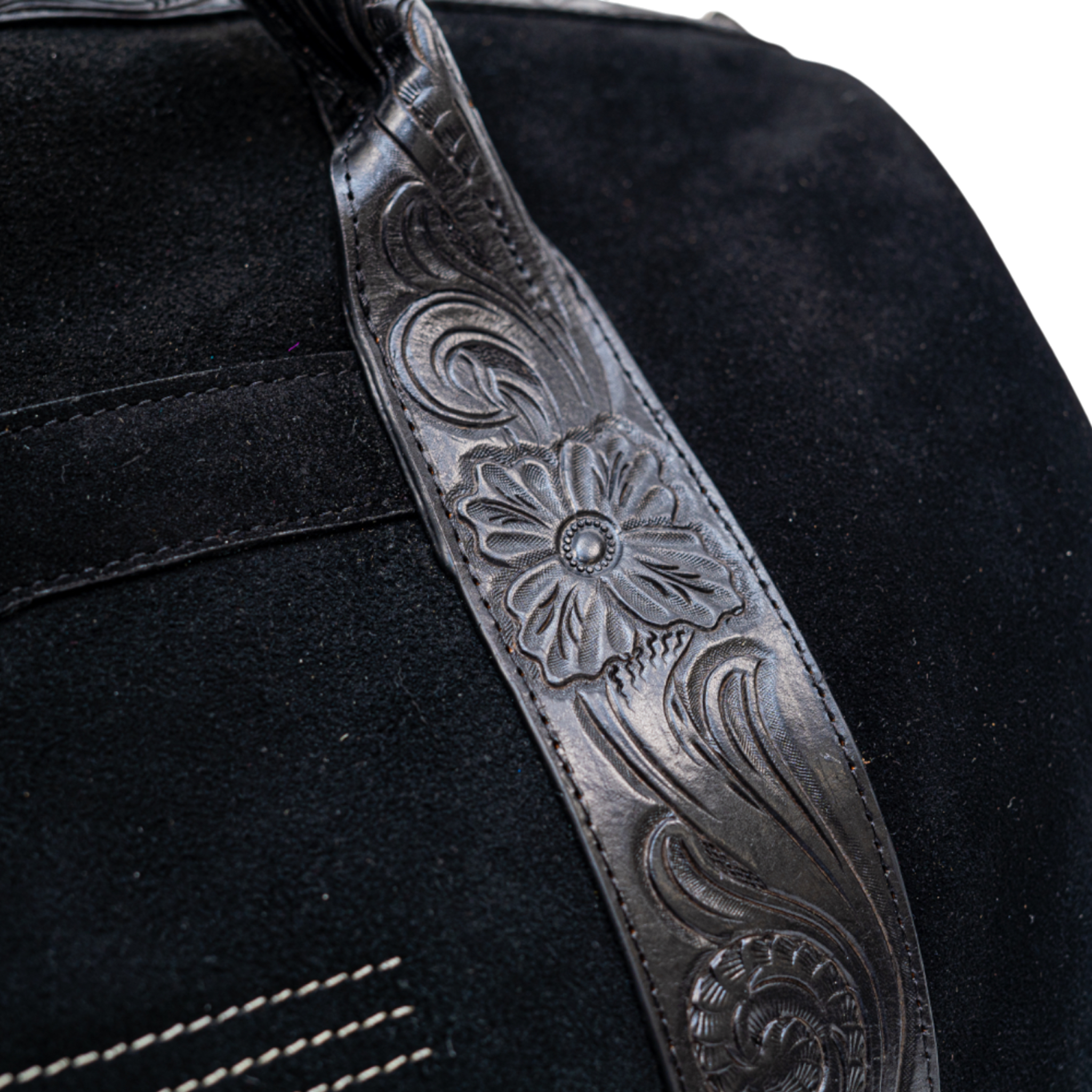 Close-up of a black leather guitar strap with floral embossing on a black background