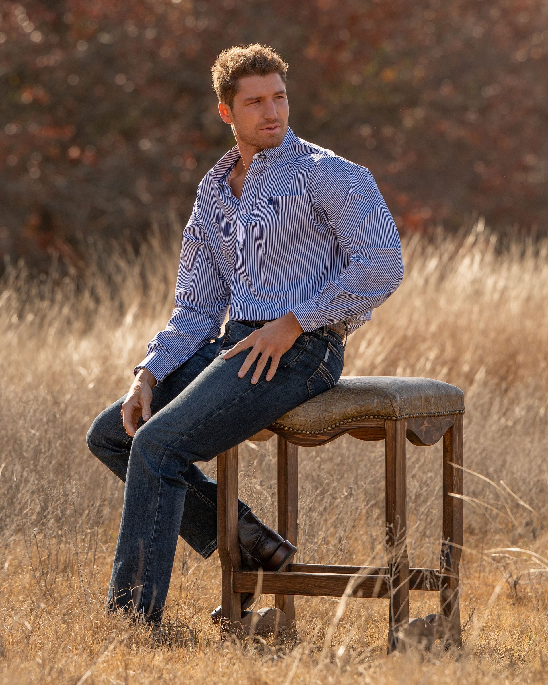 Man sitting on a wooden stool in a field with trees in the background