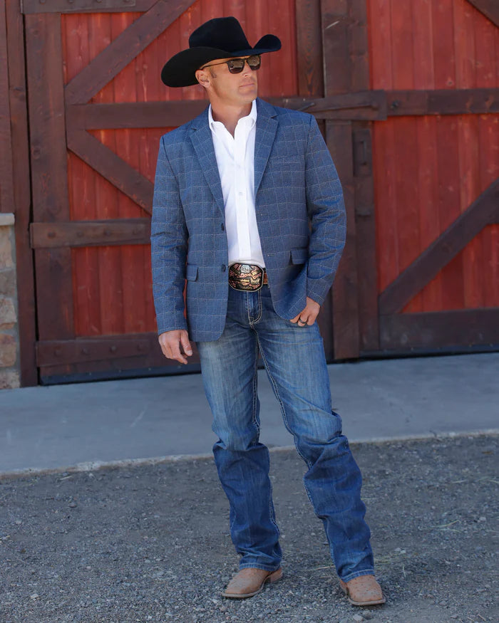 Man in cowboy attire standing in front of a red barn door.
