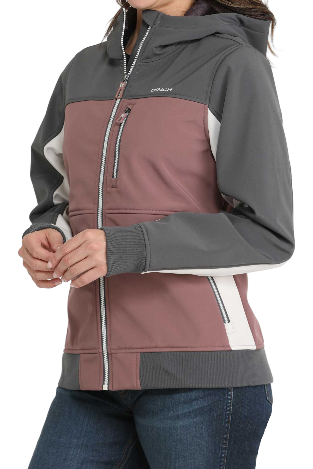 A woman wearing a color-blocked jacket with mauve, gray, and white panels, paired with blue jeans