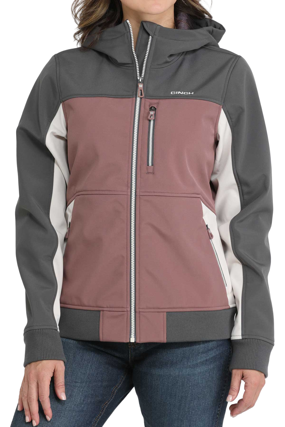 A woman wearing a color-blocked jacket with mauve, gray, and white panels, paired with blue jeans