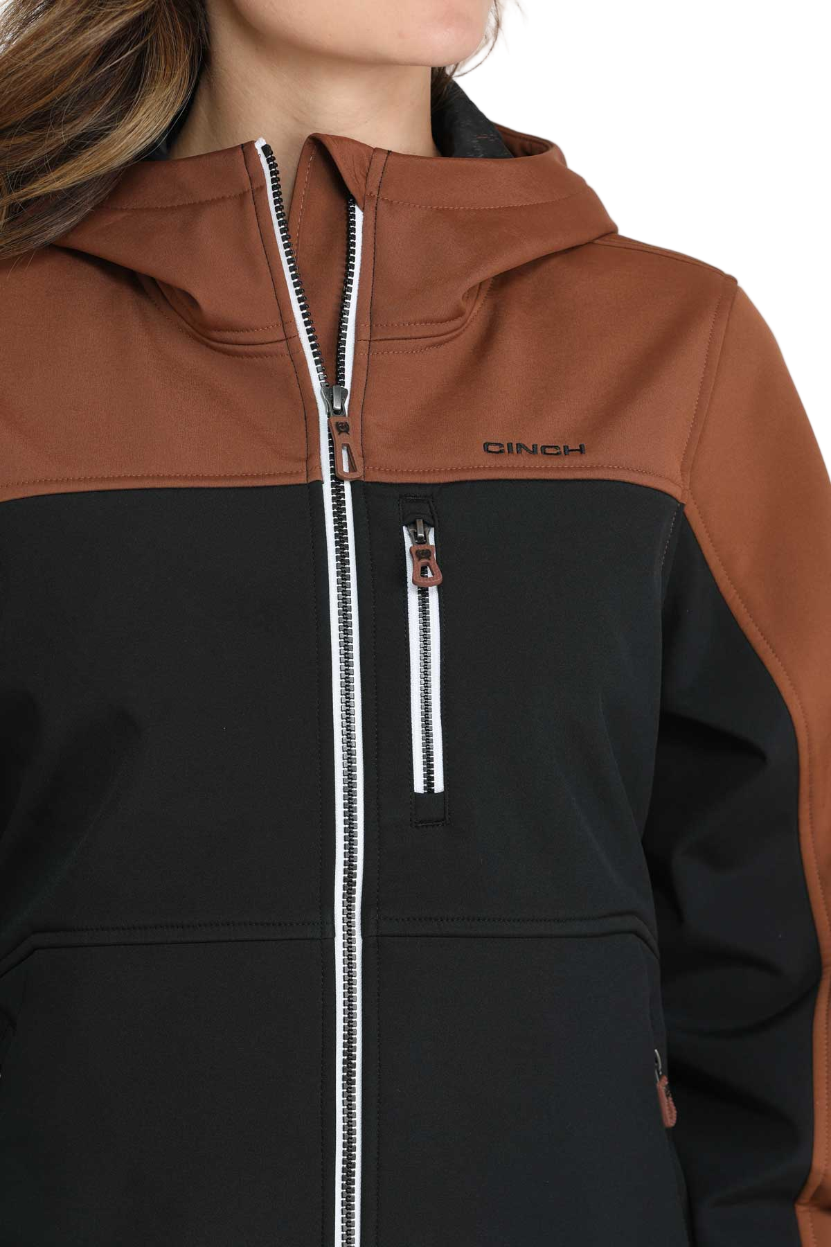 Woman wearing a two-tone hooded jacket with a brown upper section and sleeves and a black lower body. The jacket features a full front zipper, white contrast stitching, and zippered pockets.