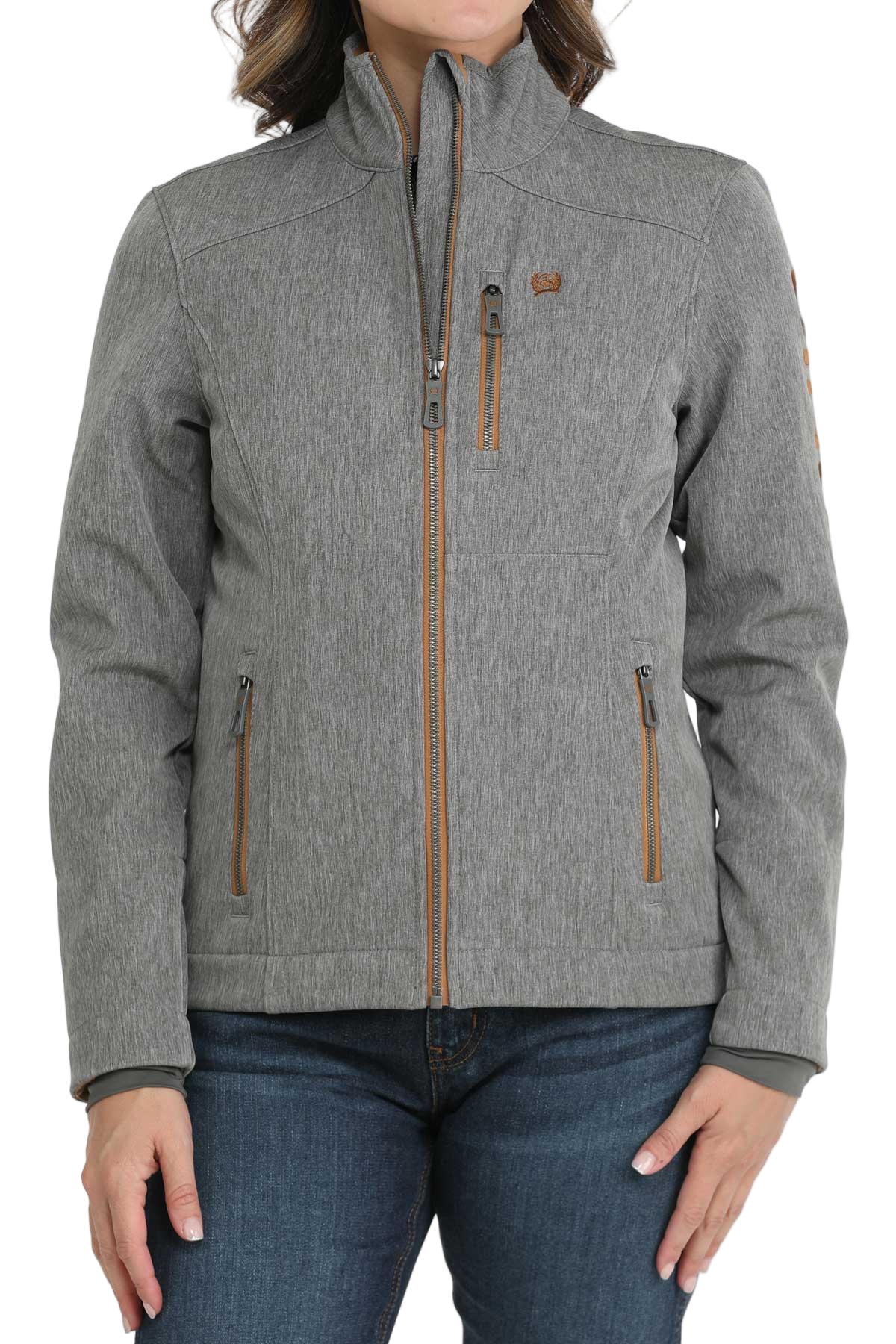 A woman wearing a light gray softshell jacket with brown zipper accents paired with dark blue jeans