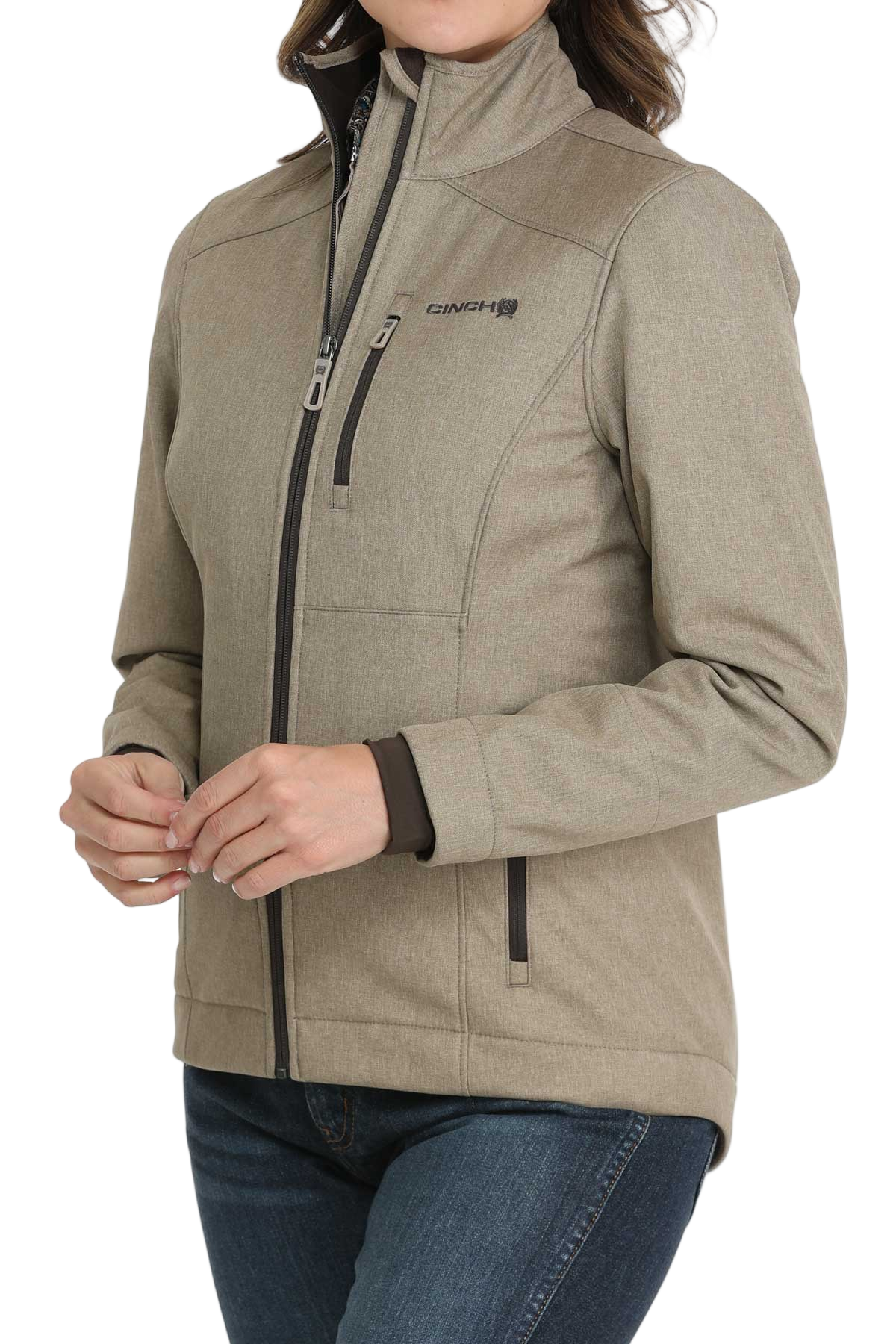 A woman wearing a light olive zip-up jacket with a high collar and front pockets, paired with dark jeans