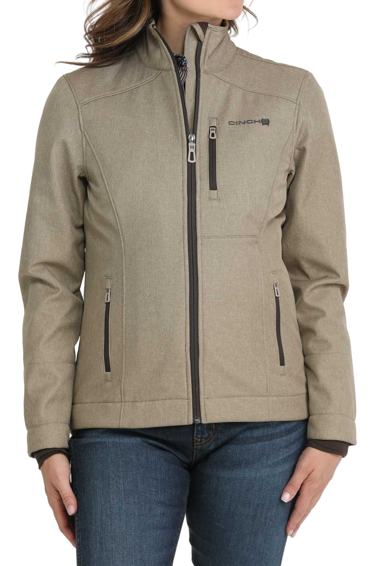 A woman wearing a light olive zip-up jacket with a high collar and front pockets, paired with dark jeans