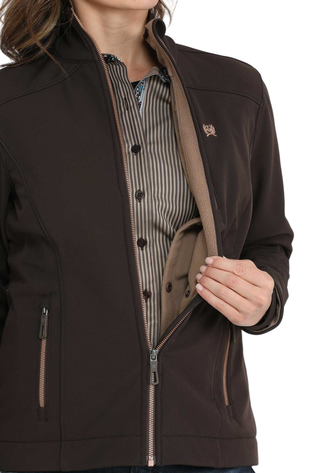 Woman wearing a dark brown softshell jacket, holding it open to show the inside pocket, revealing a striped shirt underneath
