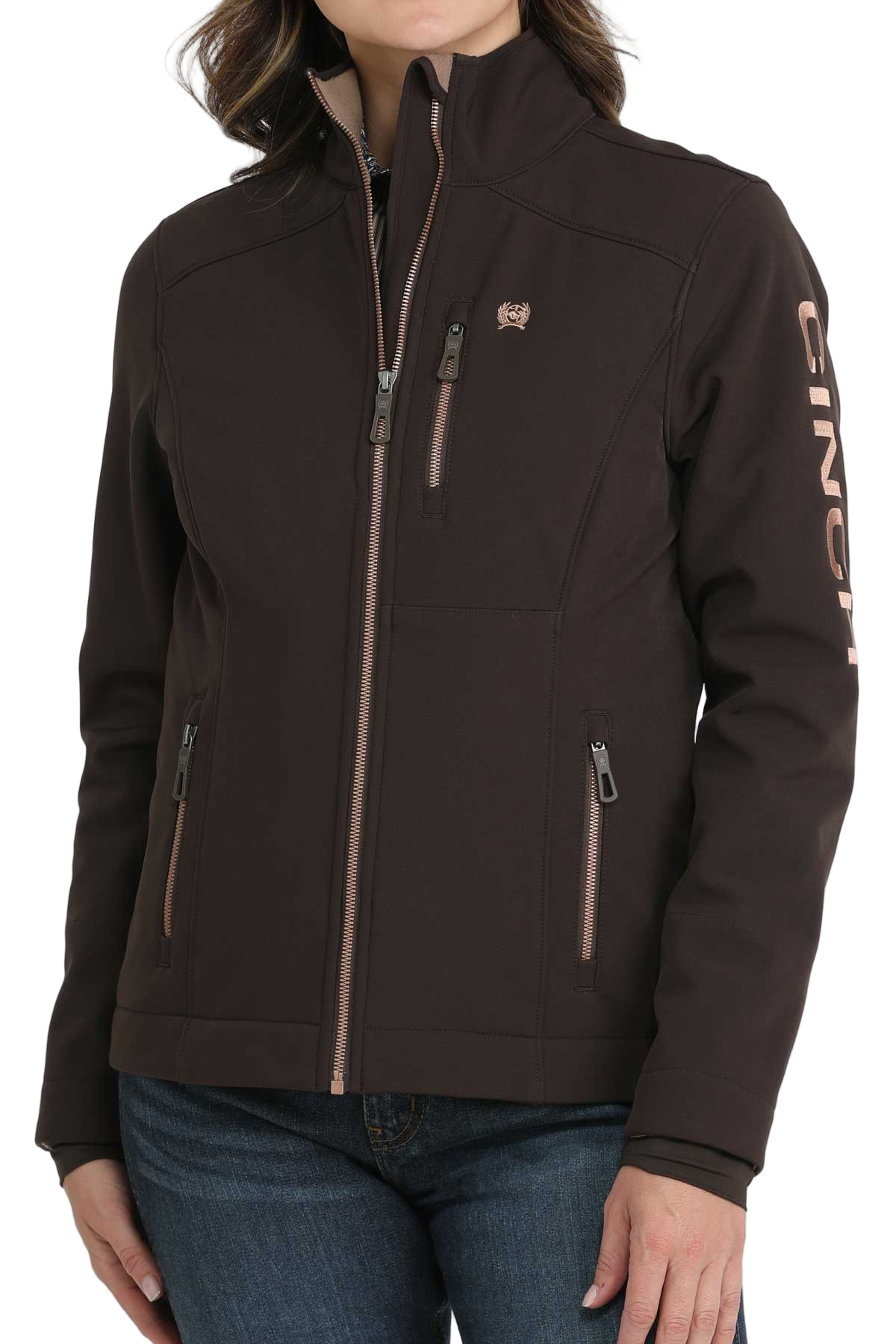 Woman wearing a dark brown CINCH softshell jacket with a front zipper and jeans