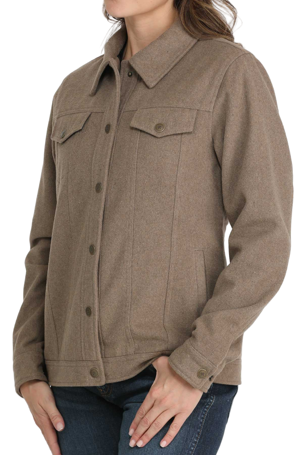 A woman wearing a taupe button-up jacket with flap chest pockets and long sleeves, paired with blue jeans
