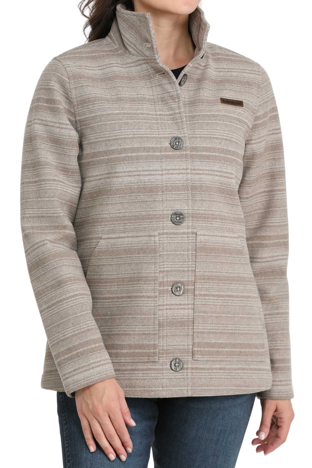 Woman wearing a beige patterned button-up jacket with a high collar, paired with dark blue jeans