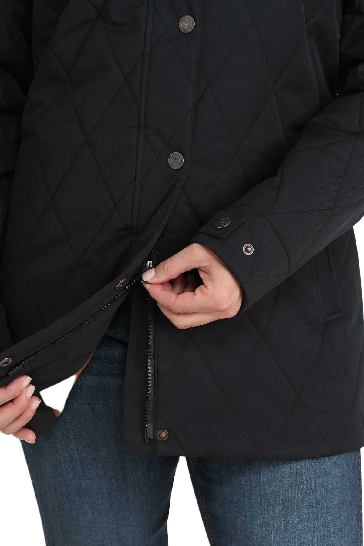 Close-up of a woman unzipping the lower section of a long black quilted jacket, showing the two-way zipper feature