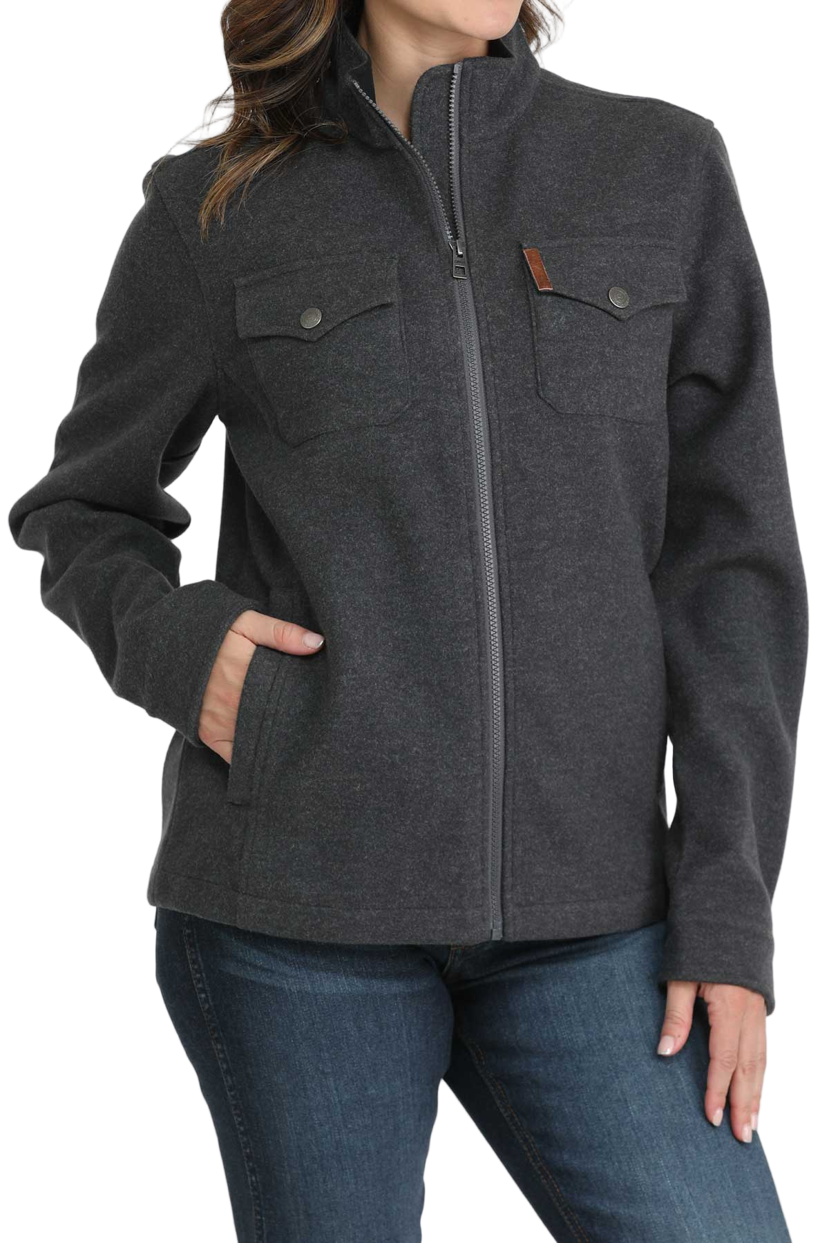 Woman wearing a dark gray zip-up jacket with flap chest pockets and side pockets, paired with blue jeans. The jacket has a high collar and a simple, casual design