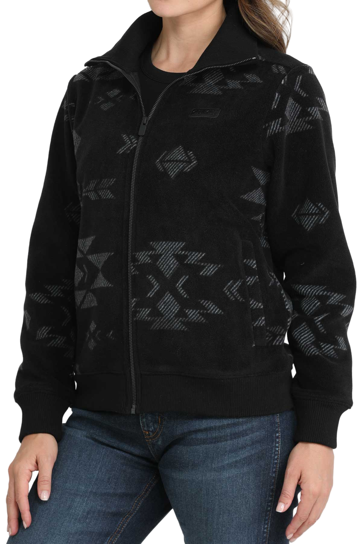 A woman wearing a black zip-up jacket with a subtle gray southwest-style pattern, paired with blue jeans