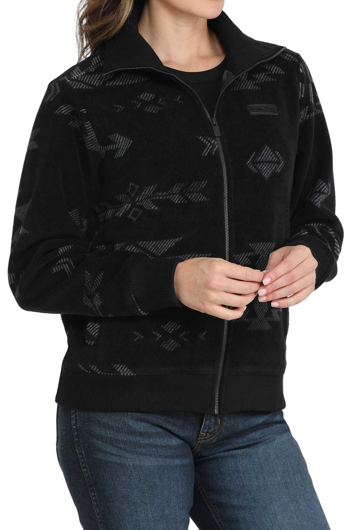 A woman wearing a black zip-up jacket with a subtle gray southwest-style pattern, paired with blue jeans