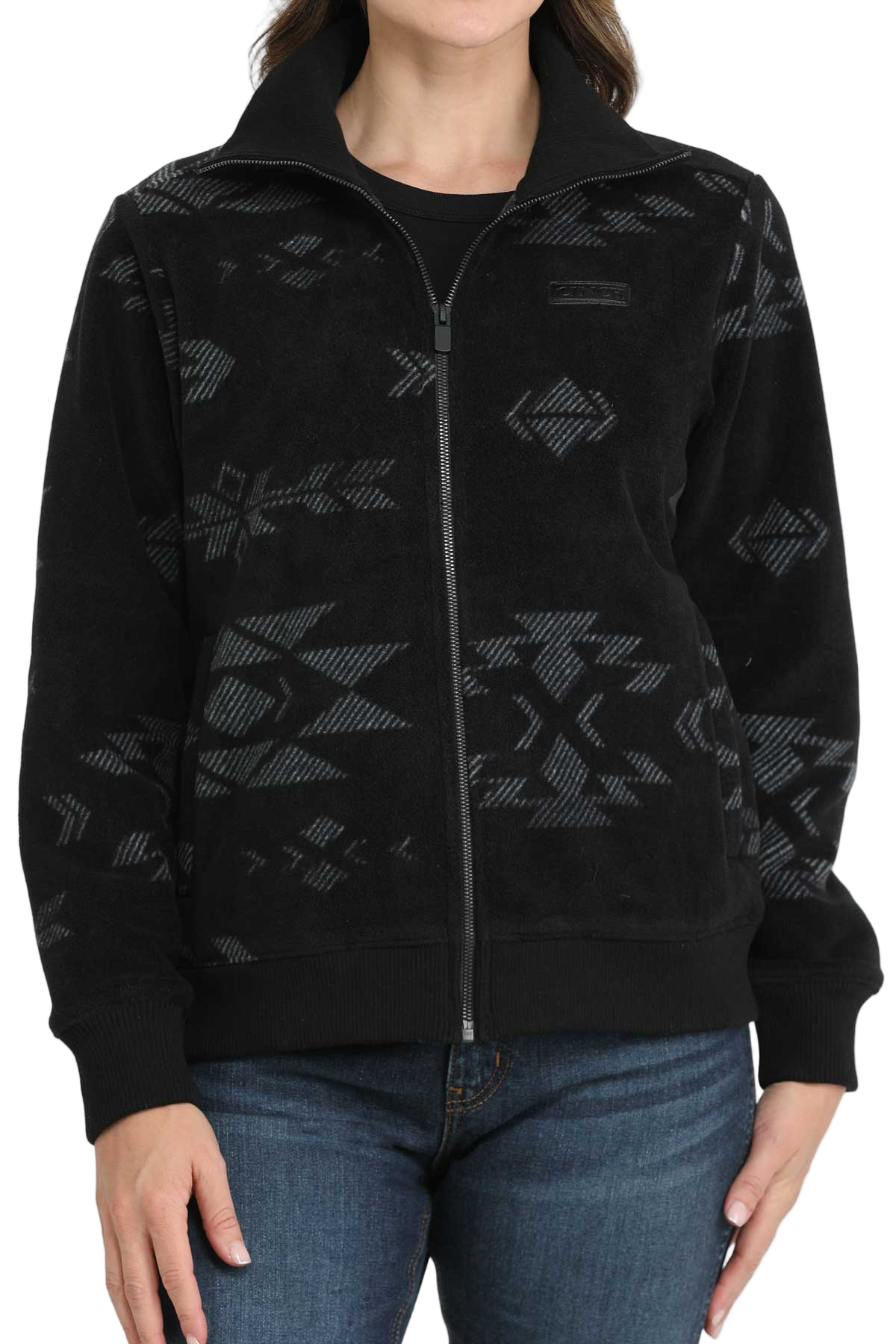 A woman wearing a black zip-up jacket with a subtle gray southwest-style pattern, paired with blue jeans