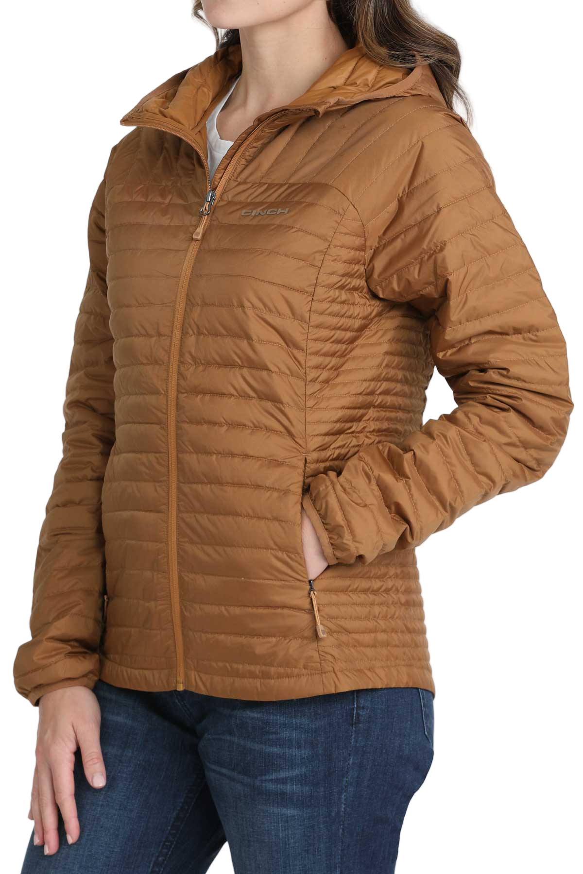 Woman wearing a light brown quilted puffer jacket with her hands in the front pockets, paired with dark blue jeans