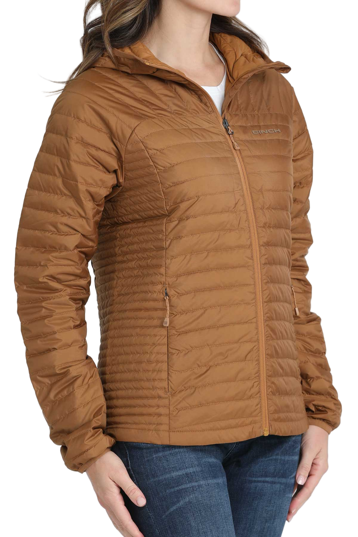 Woman wearing a light brown quilted puffer jacket with her hands in the front pockets, paired with dark blue jeans