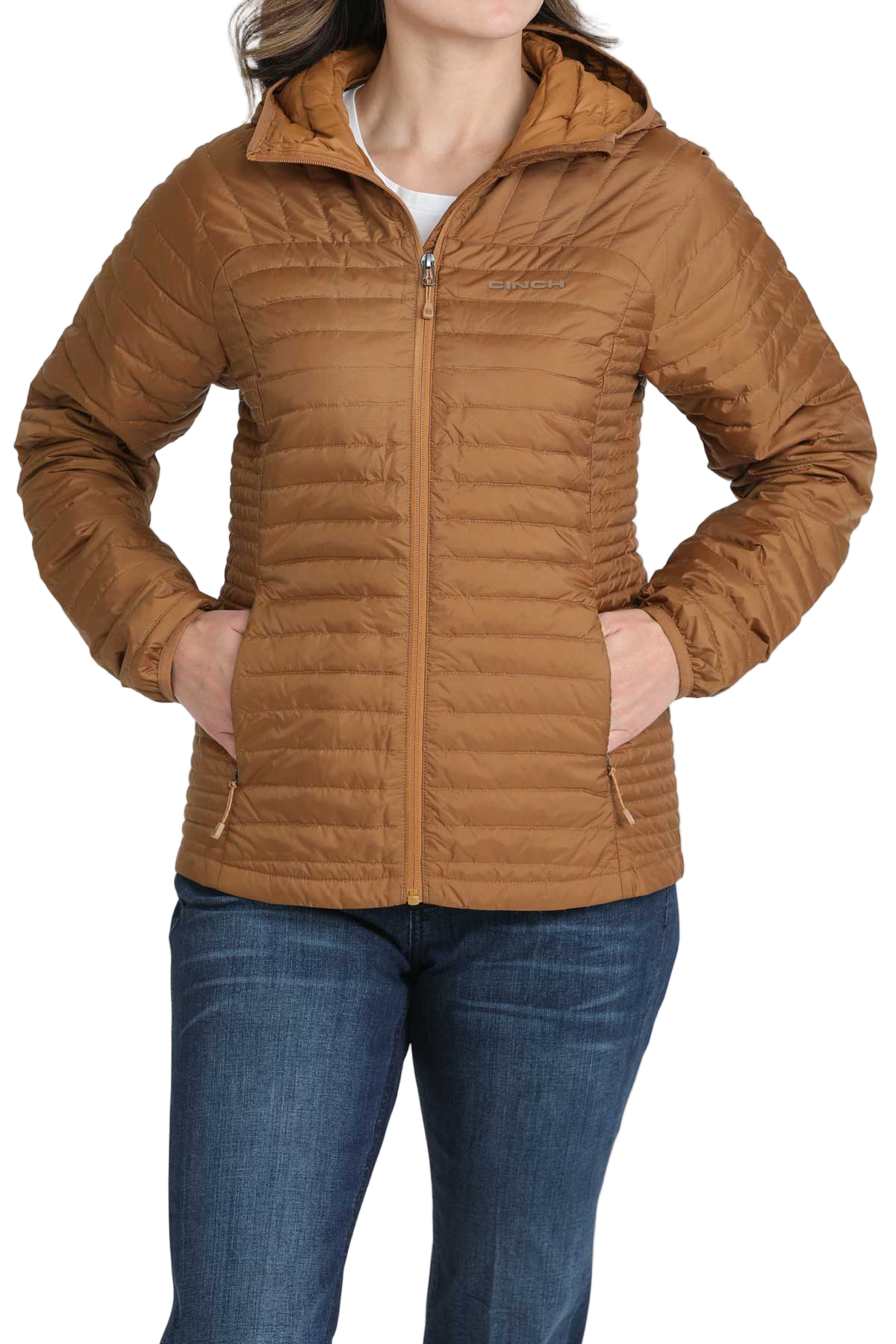Woman wearing a light brown quilted puffer jacket with her hands in the front pockets, paired with dark blue jeans