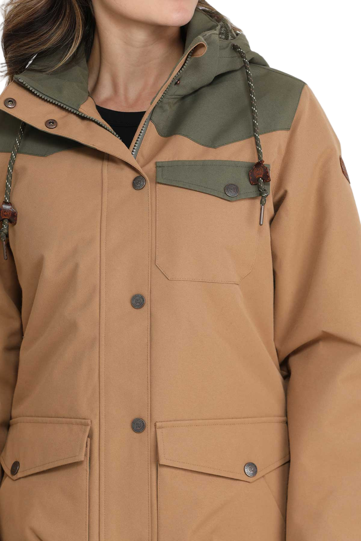 Woman wearing a tan and olive green hooded jacket with front pockets and button closures