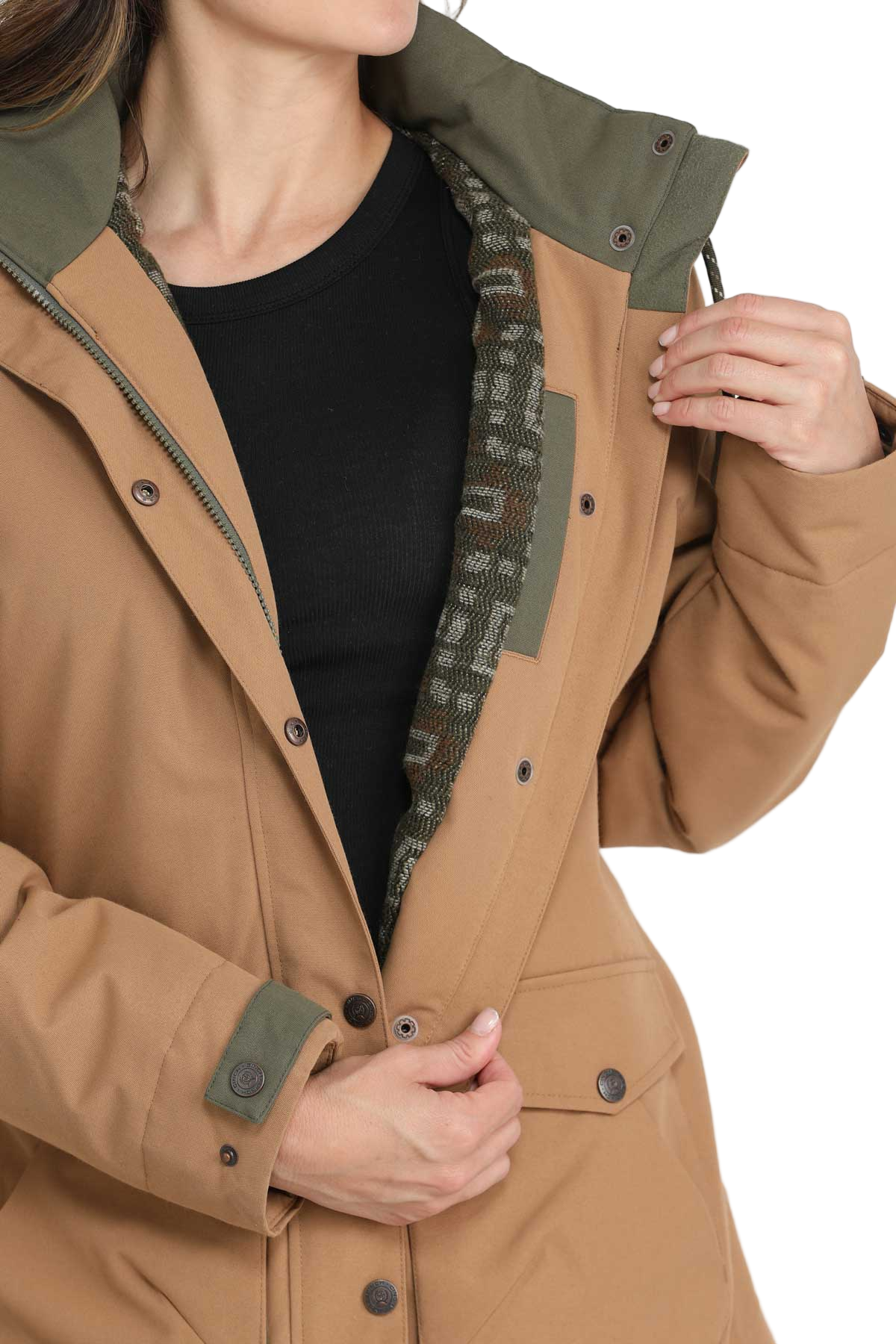 Close-up of a woman opening a tan jacket to show its inner lining, which features a geometric pattern. The jacket has an olive green hood and trim, snap buttons, and a black shirt underneath