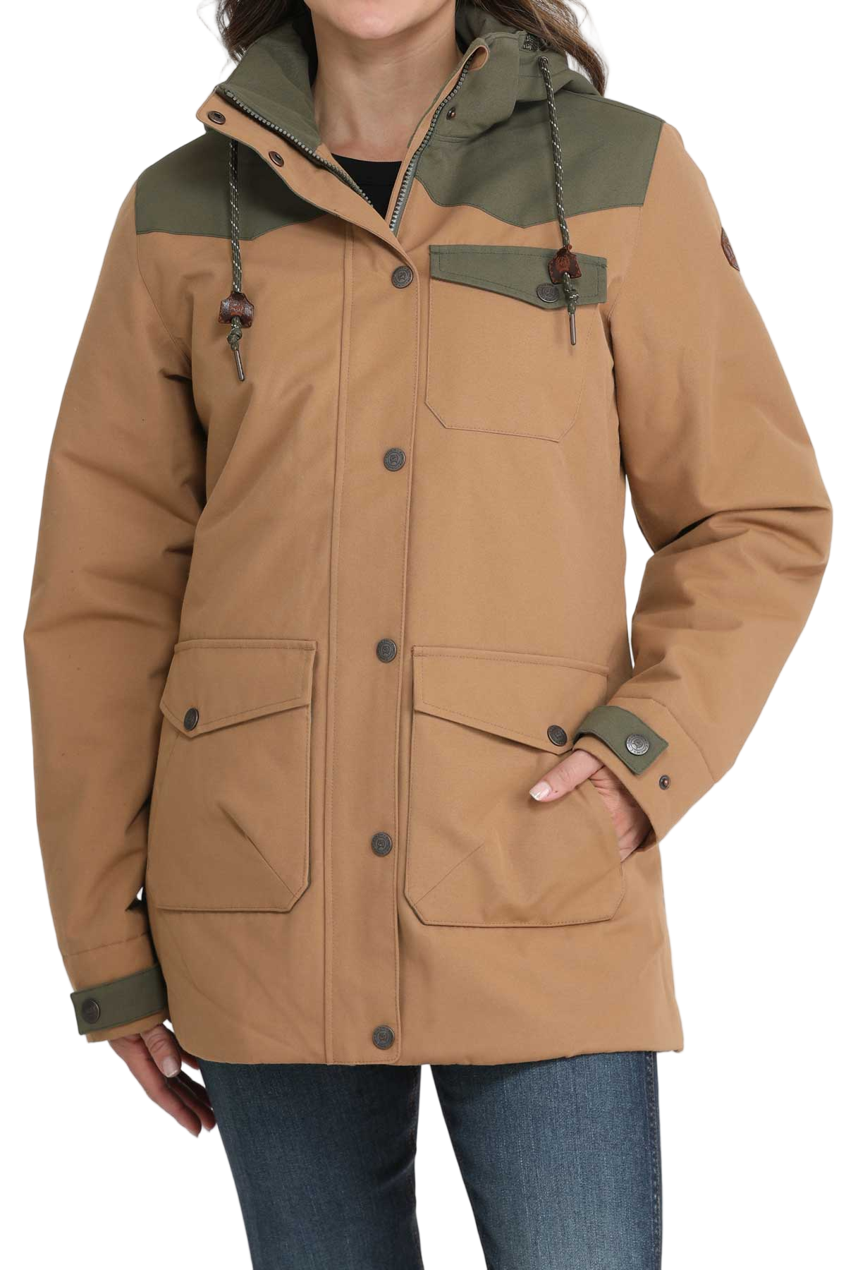 Woman wearing a tan and olive green hooded jacket with front pockets and button closures, paired with dark denim jeans