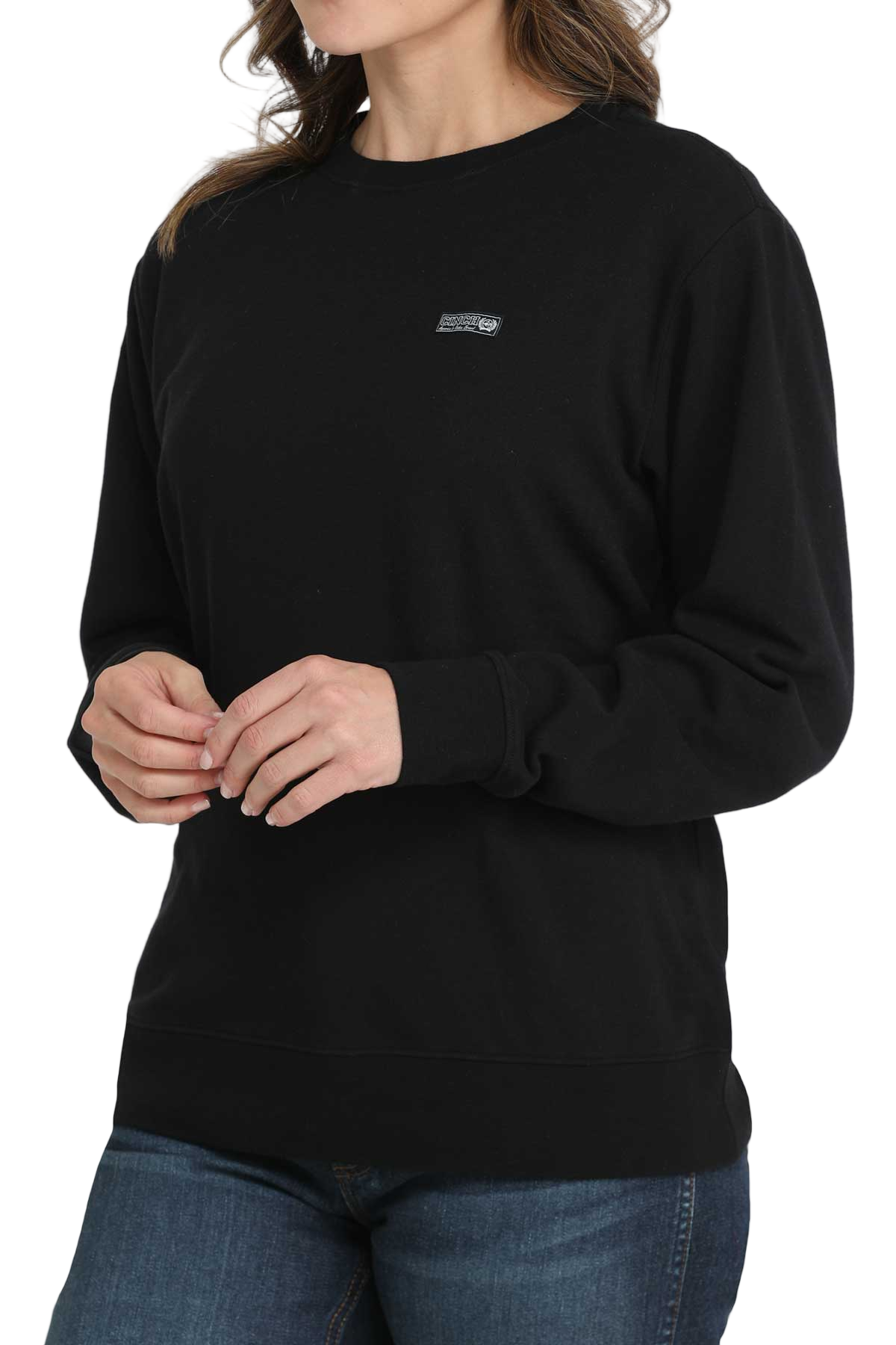 Woman wearing a black crewneck sweatshirt with a small embroidered logo on the chest, paired with blue jeans