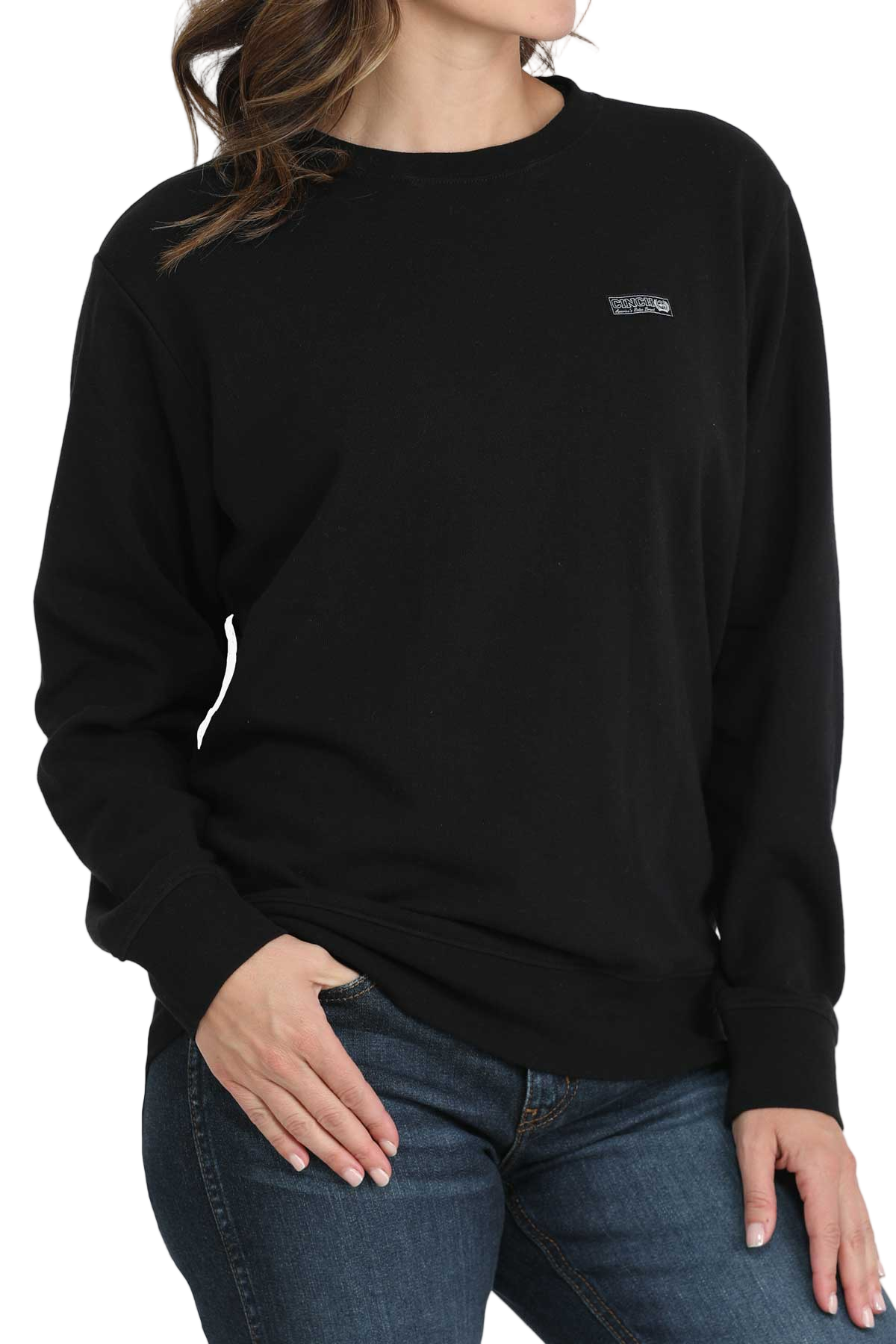 Woman wearing a black crewneck sweatshirt with a small embroidered logo on the chest, paired with blue jeans
