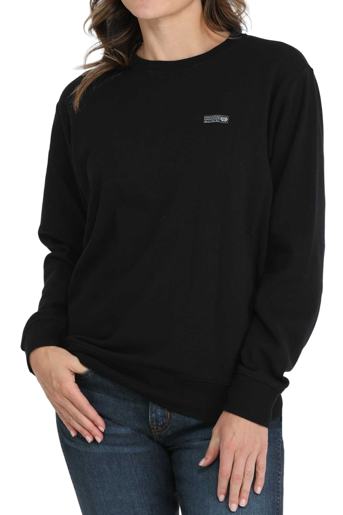 Woman wearing a black crewneck sweatshirt with a small embroidered logo on the chest, paired with blue jeans