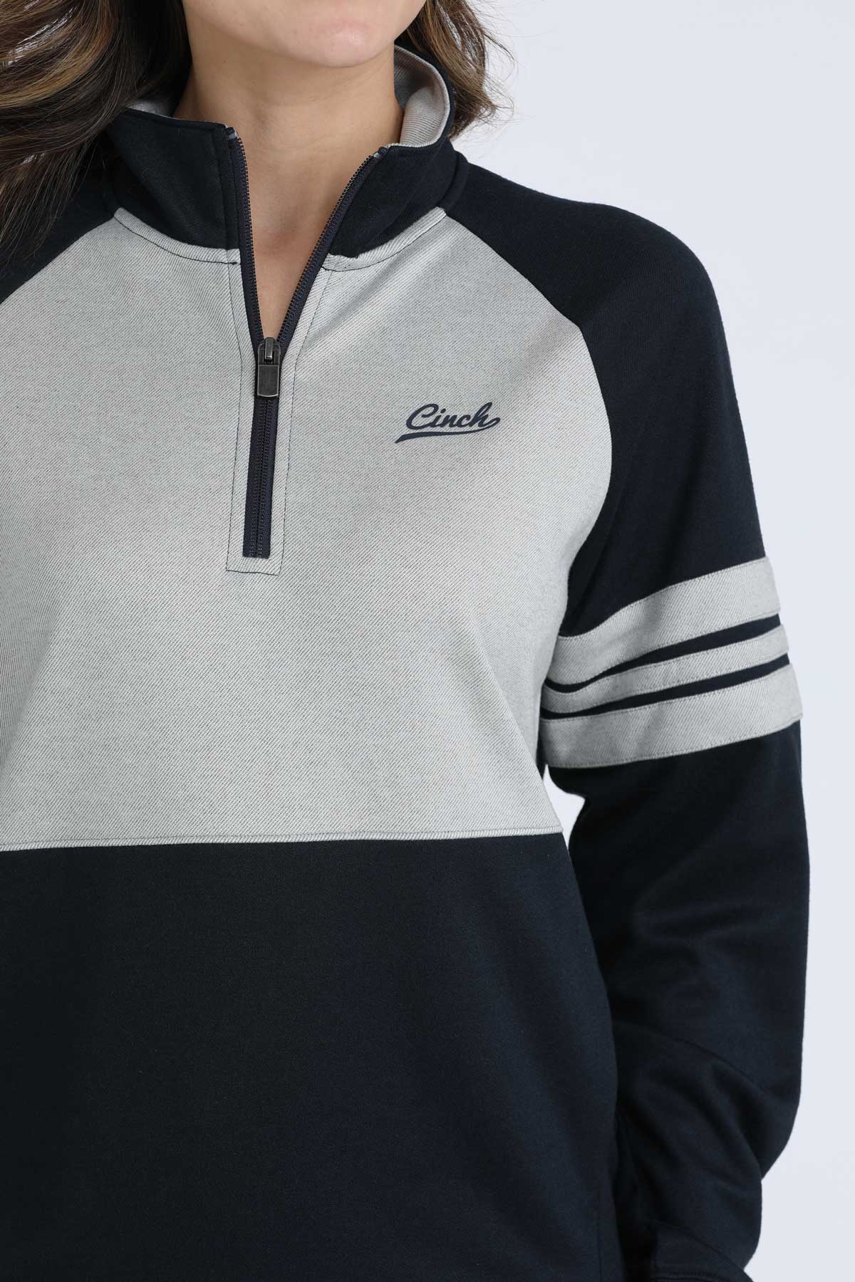 Woman wearing a navy and grey Cinch 1/4 zip sweatshirt with striped sleeves