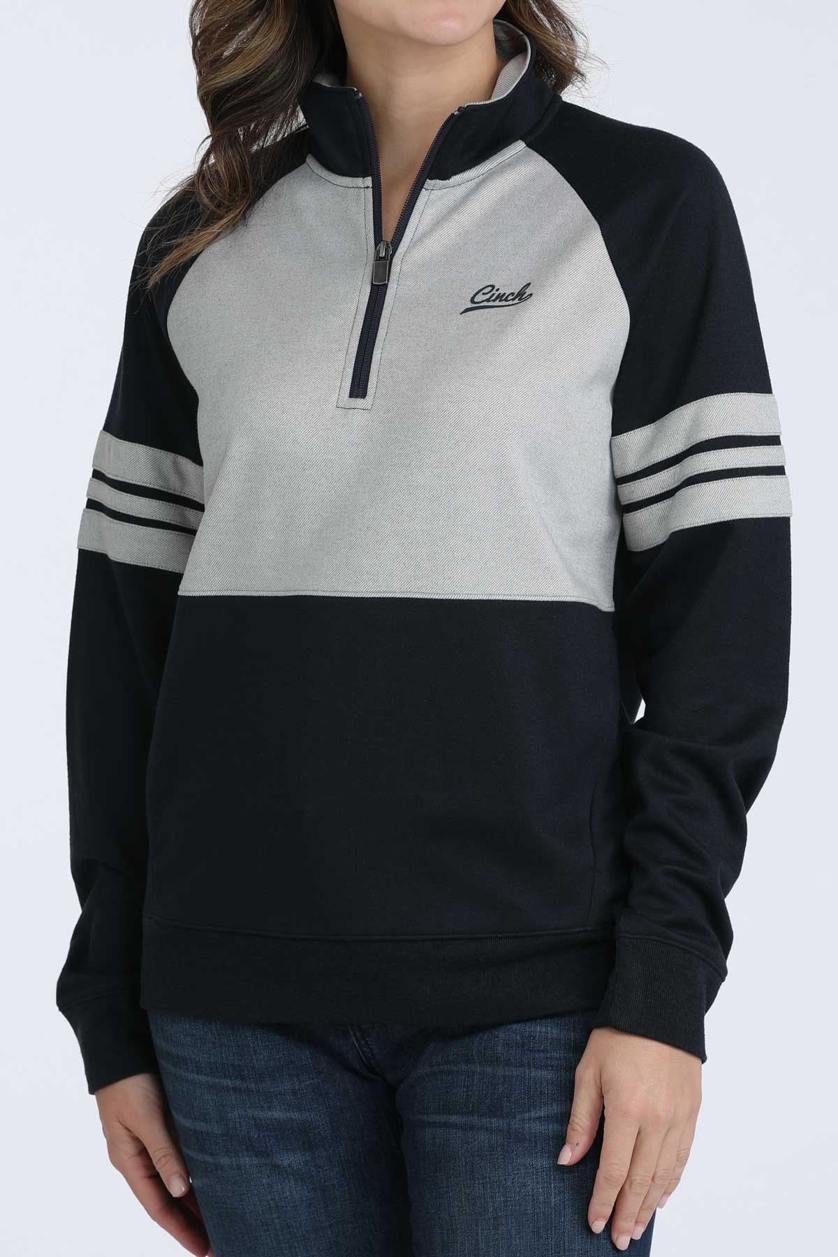 Woman wearing a navy and grey Cinch 1/4 zip sweatshirt with striped sleeves and jeans on a white background