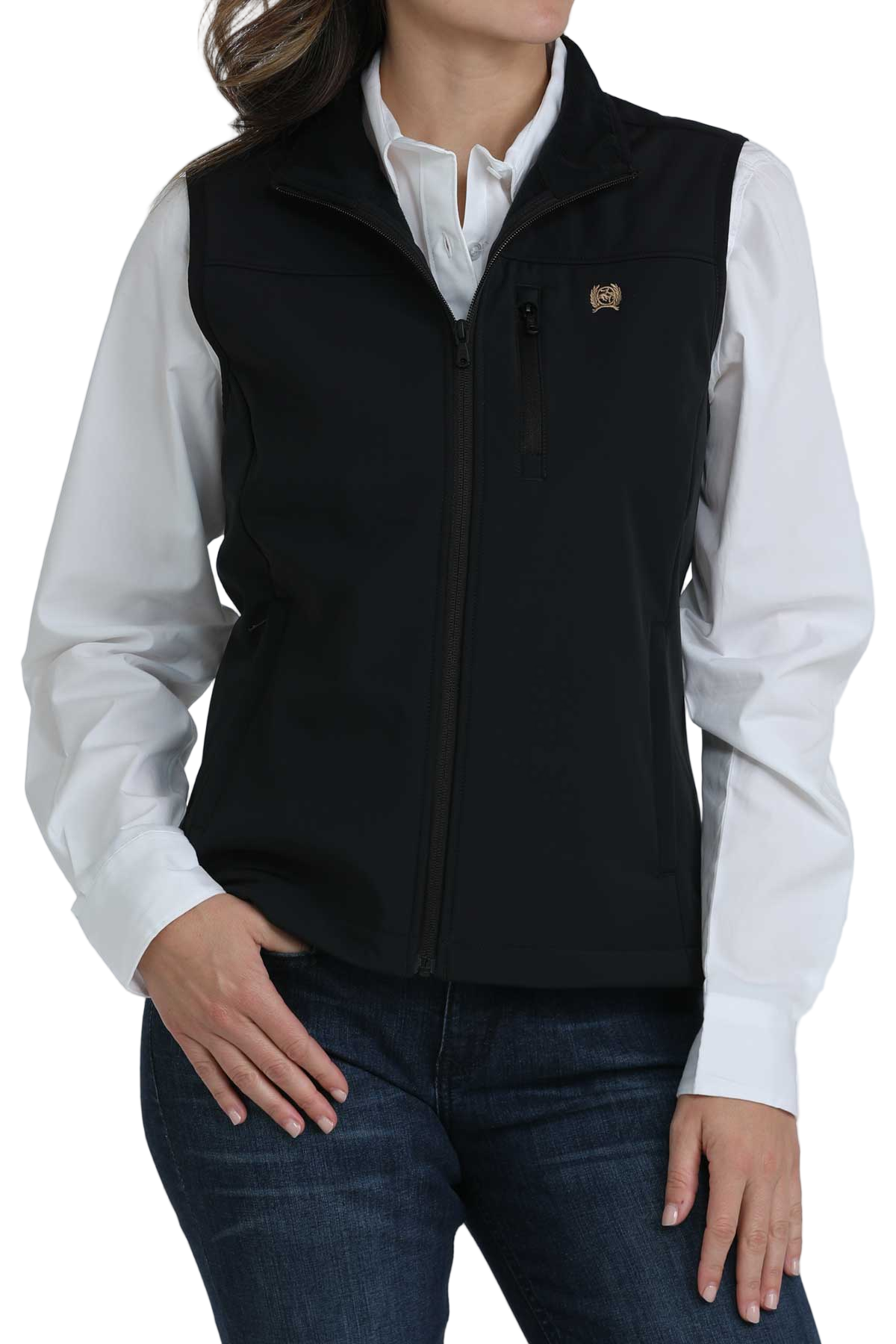 Woman wearing a black zip-up softshell vest over a white button-down shirt, paired with dark blue jeans. The vest has a high collar and zippered pockets