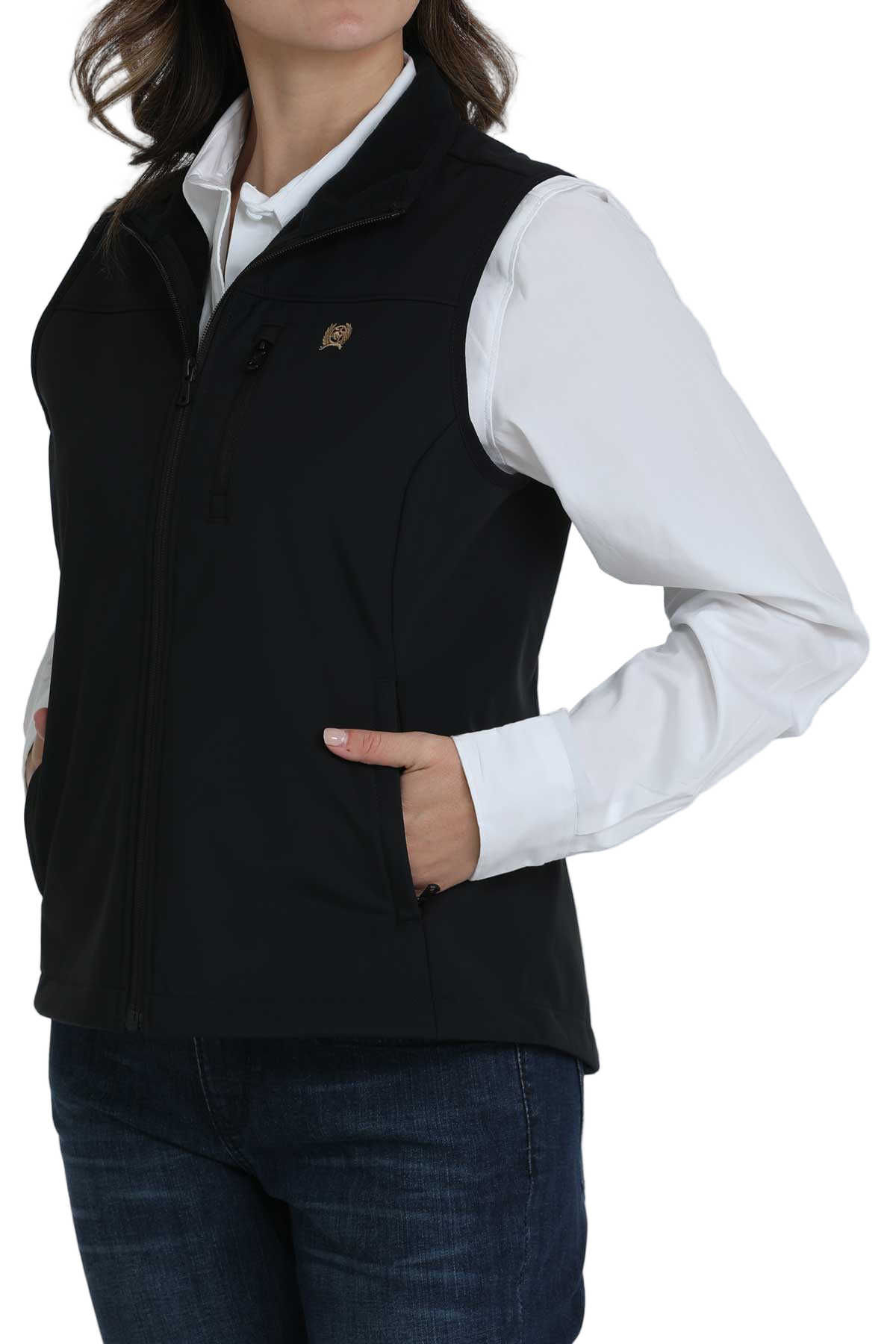 Woman wearing a black zip-up softshell vest over a white button-down shirt, paired with dark blue jeans. The vest has a high collar and zippered pockets