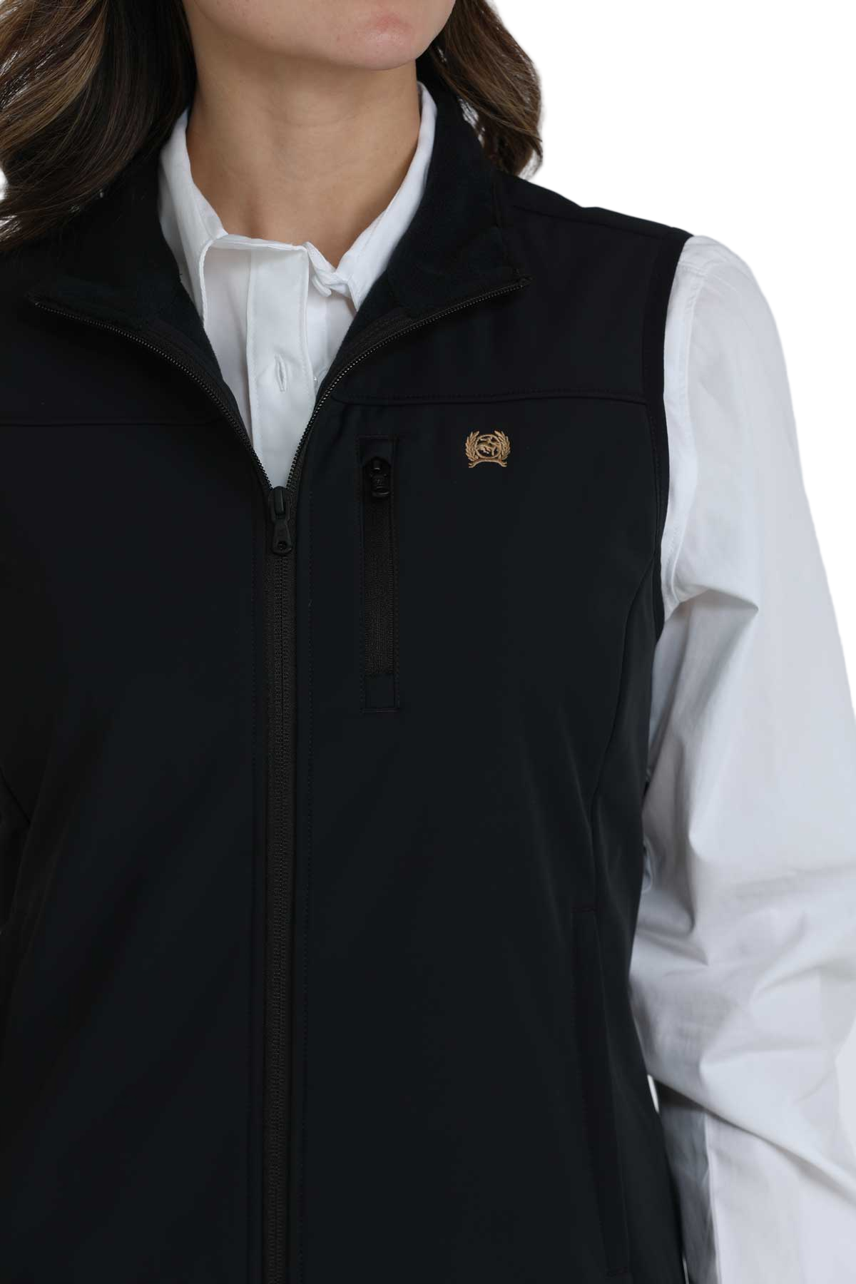 Woman wearing a black zip-up softshell vest over a white button-down shirt. The vest has a high collar and zippered pockets