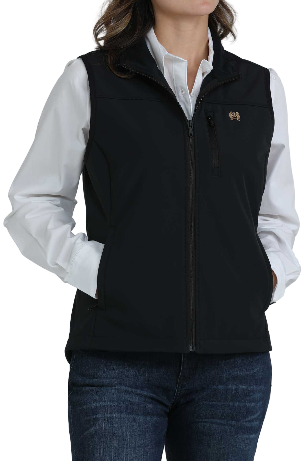 Woman wearing a black zip-up softshell vest over a white button-down shirt, paired with dark blue jeans. The vest has a high collar and zippered pockets