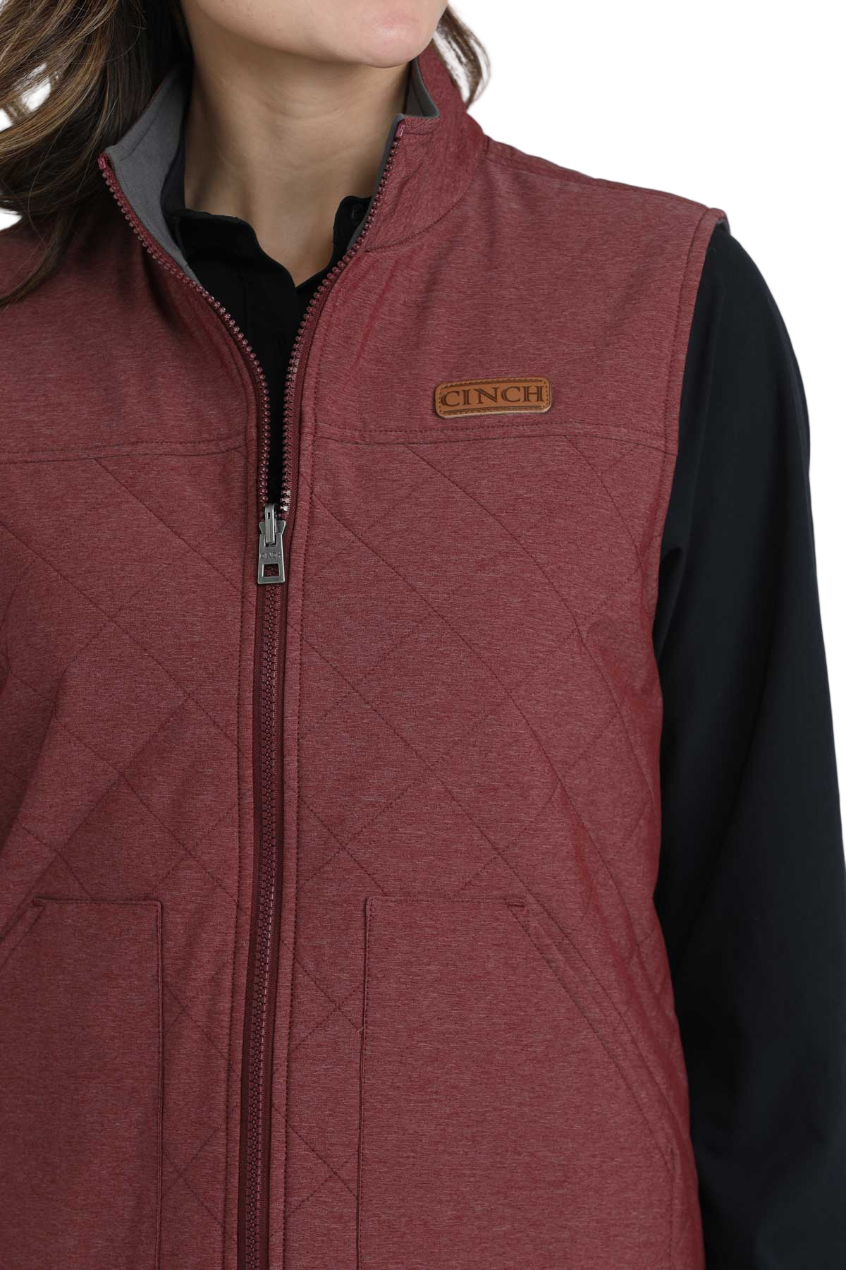 Close-up of a woman wearing a quilted burgundy zip-up vest over a black long-sleeve shirt