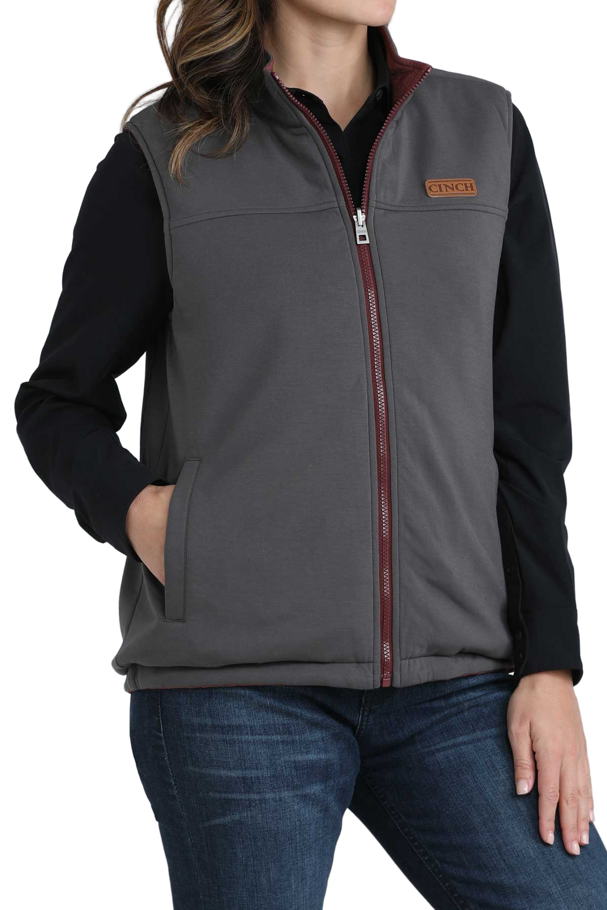 Woman wearing a grey zip-up vest with burgundy trim, layered over a black long-sleeve shirt, paired with dark blue jeans
