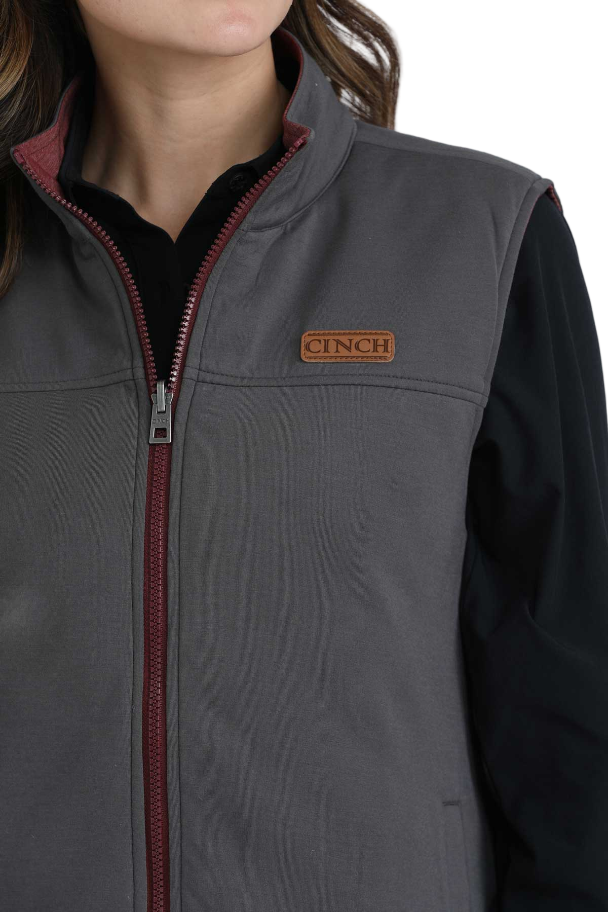 Close-up of a woman wearing a grey zip-up vest with burgundy trim, layered over a black long-sleeve shirt