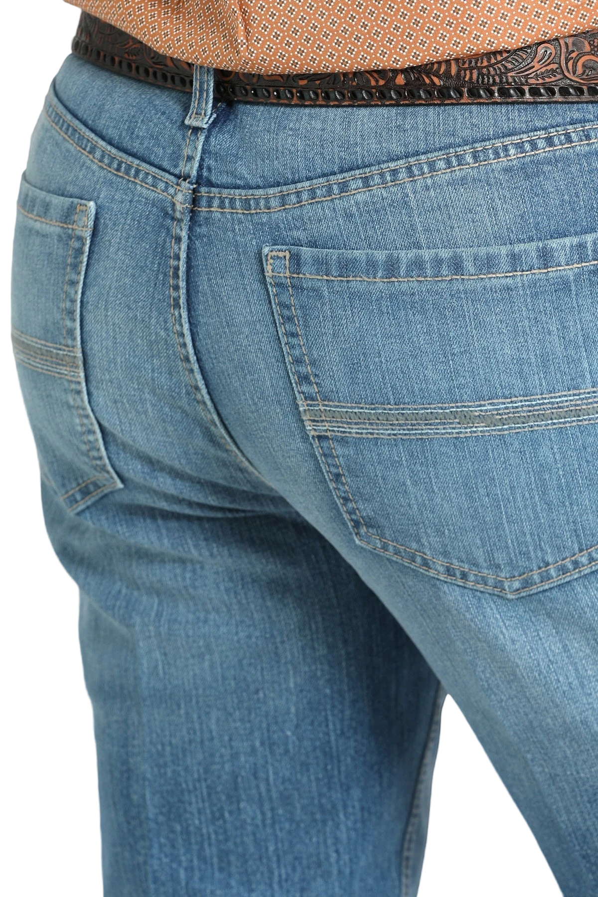 Close-up of the back of a person wearing blue denim jeans with simple stitching on the back pockets and a tooled brown leather belt, paired with a tucked-in patterned shirt