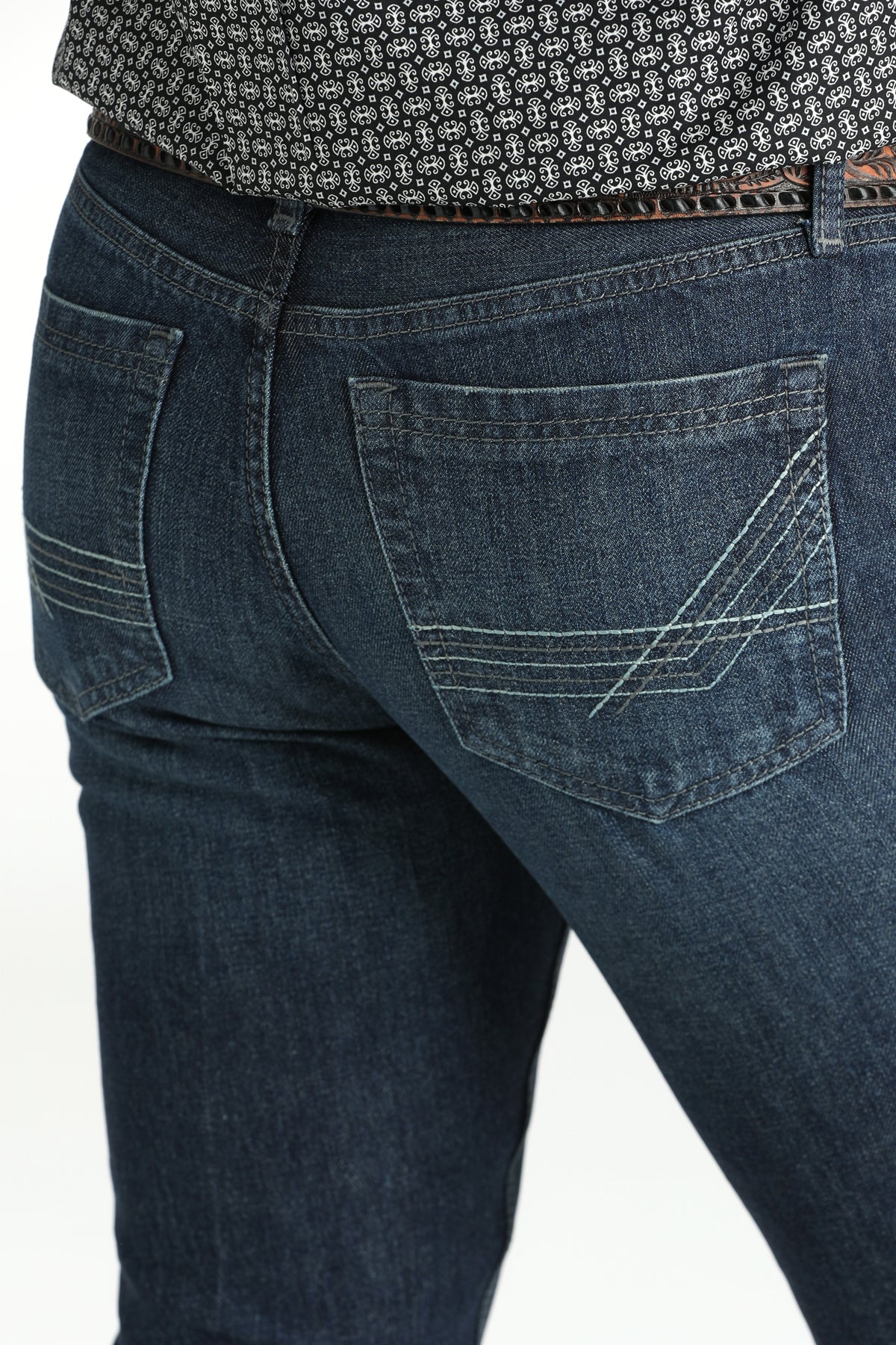 Close-up, back view of a man wearing dark wash jeans, a patterned shirt, and a belt, standing against a white background
