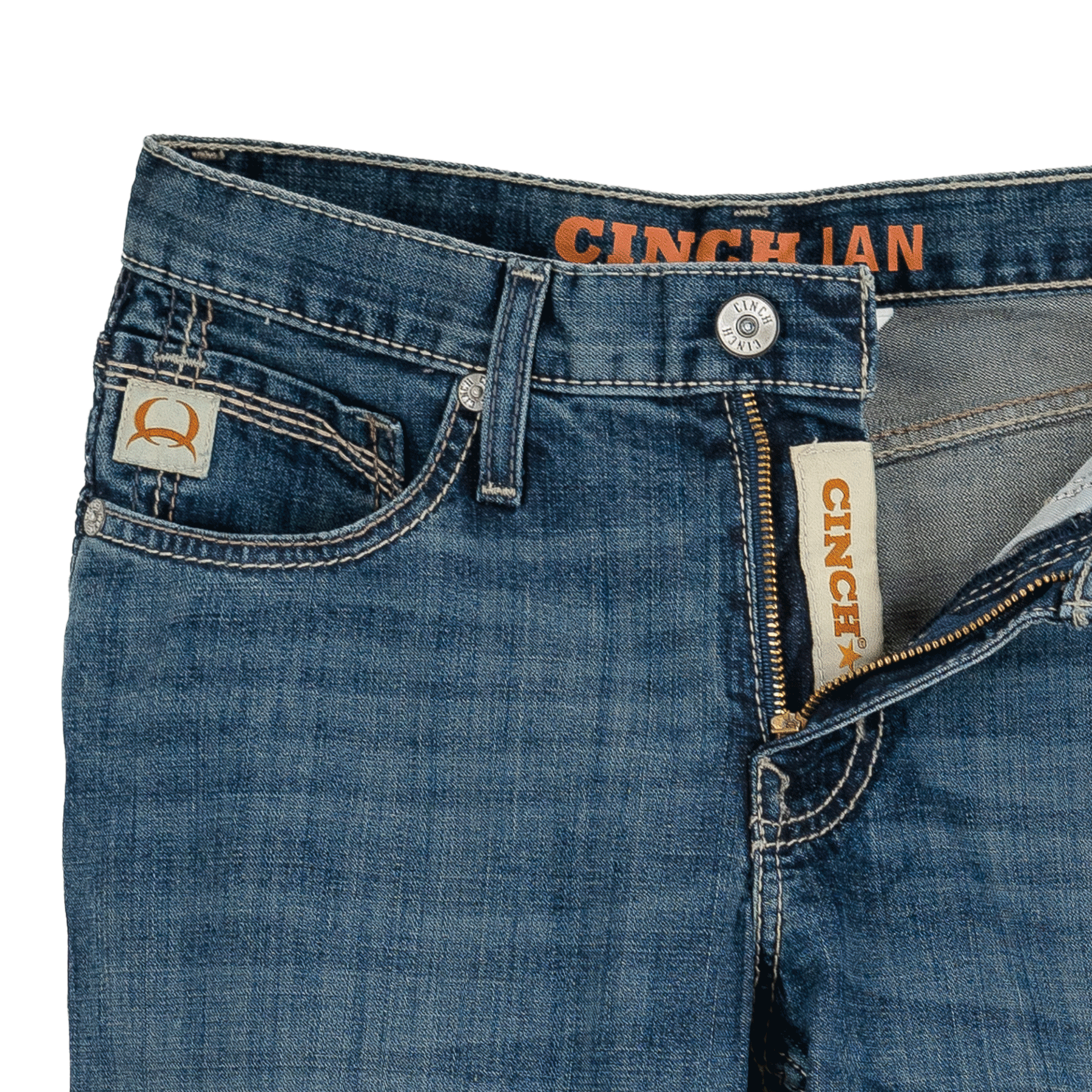 A pair of medium wash denim jeans with a partially unzipped fly, showcasing a Cinch logo on the inner waistband and a stitched patch above the coin pocket.
