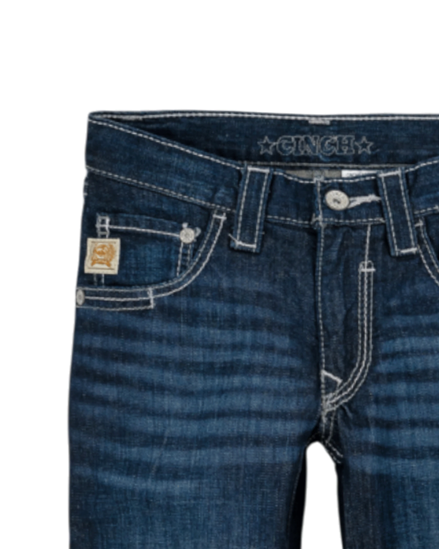 Close-up of the front of dark blue denim jeans with light fading, featuring a coin pocket with a small embroidered patch, belt loops, and a button closure with a zipper fly. The waistband has 'CINCH' stitched on it
